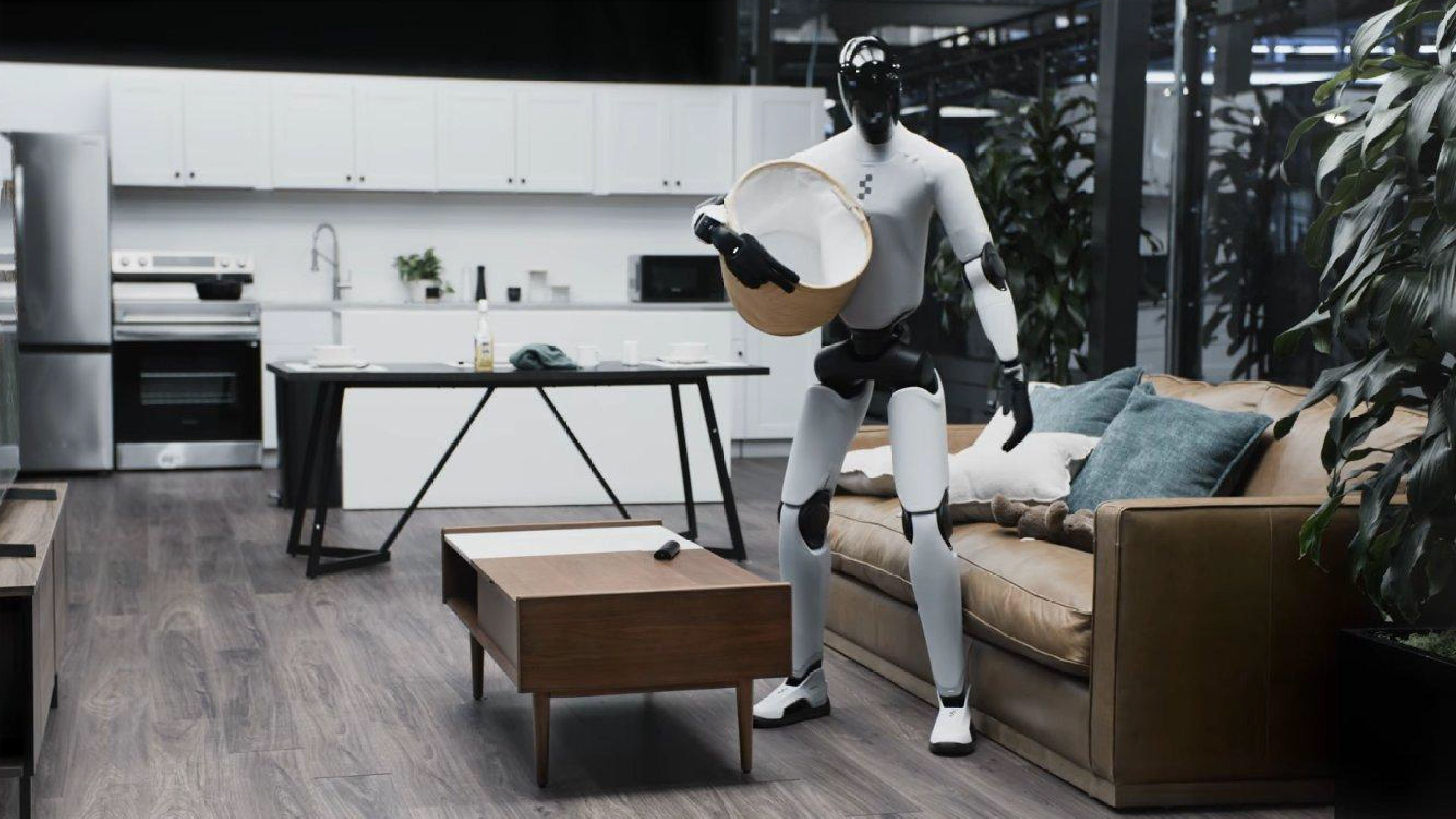 A humanoid robot carries a laundry basket in a modern home setting, standing between a living room sofa and an open kitchen.