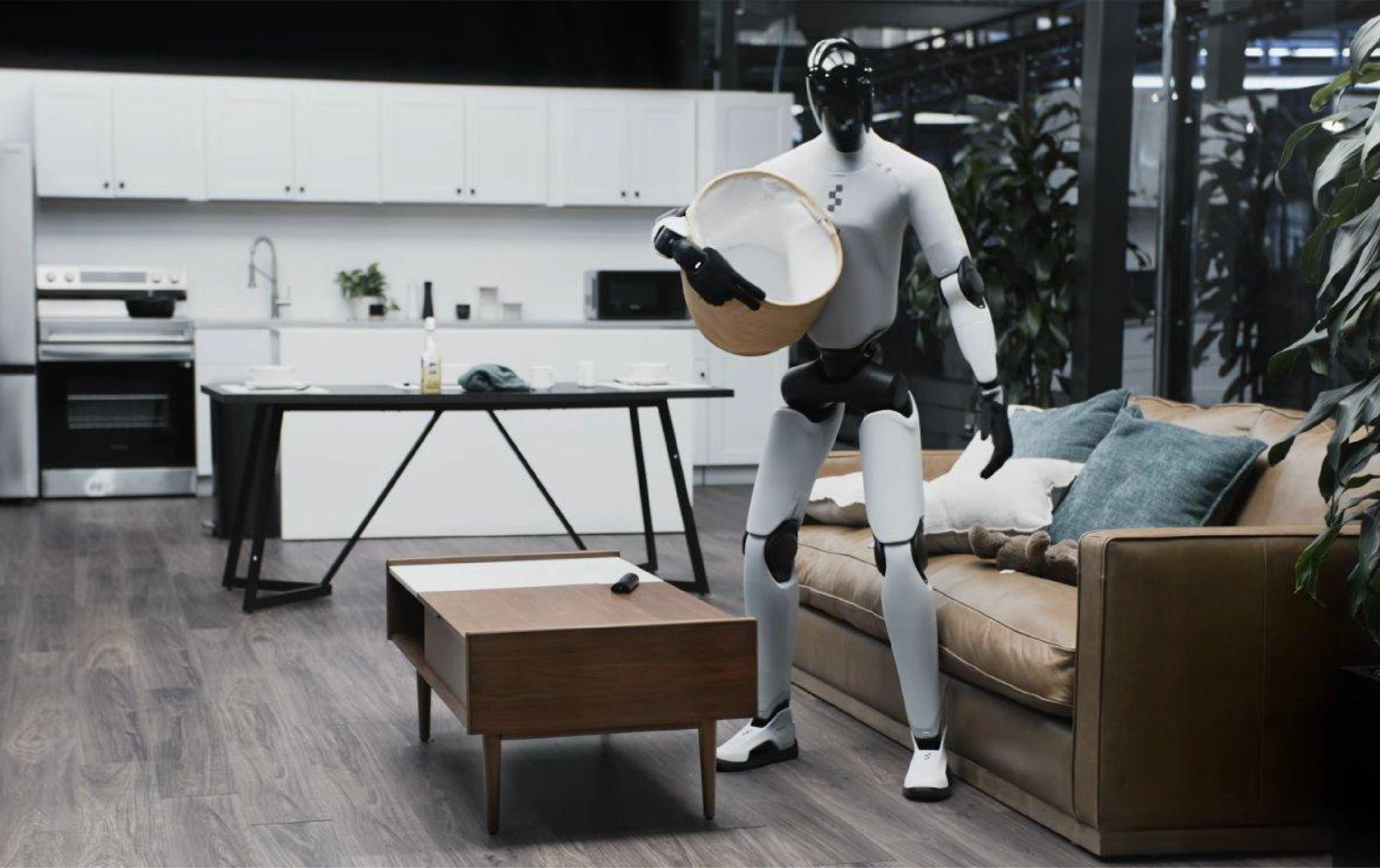 A humanoid robot carries a laundry basket in a modern home setting, standing between a living room sofa and an open kitchen.