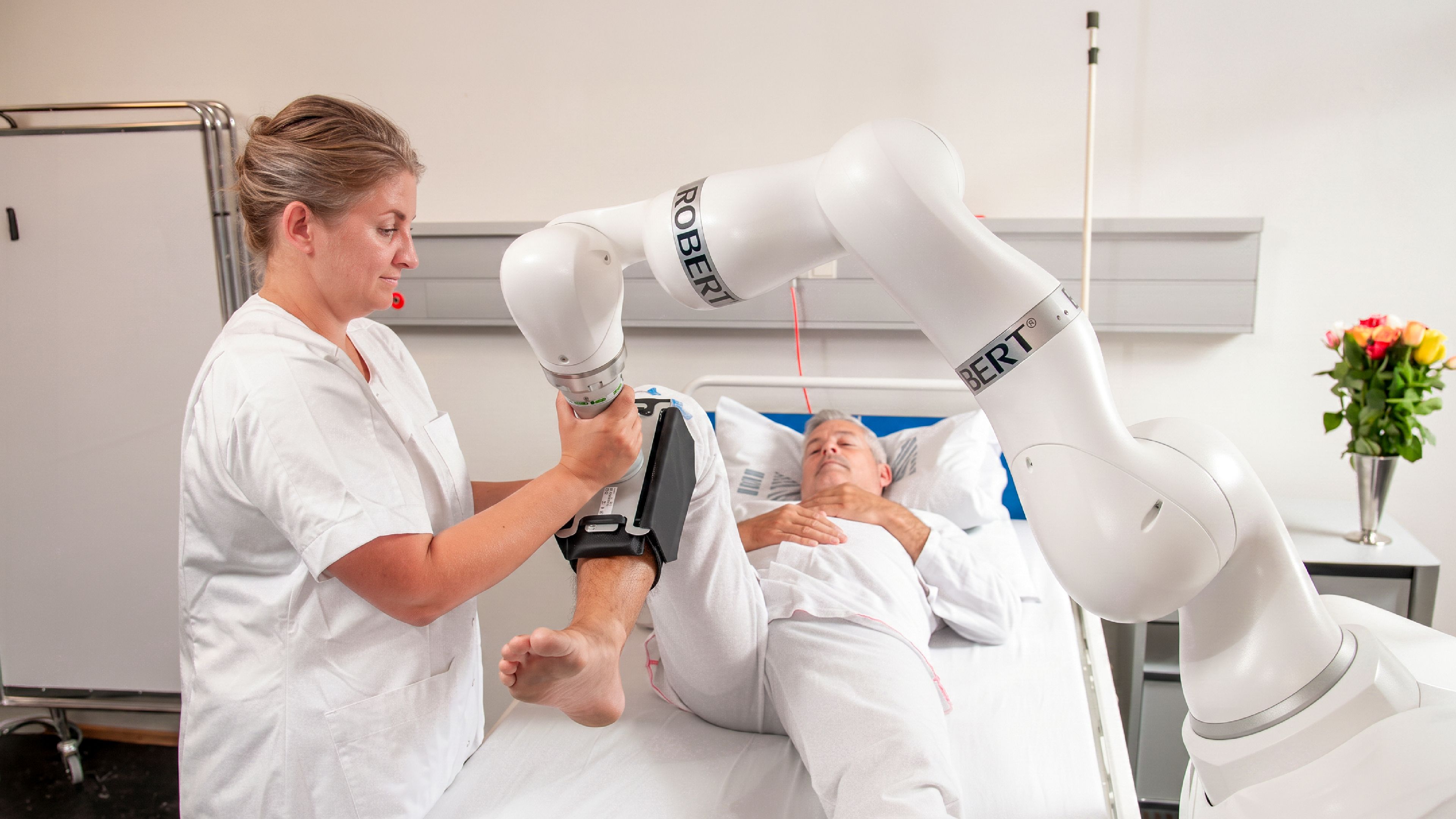 A nurse guides a ROBERT rehabilitation robot arm exercising a patient in a hospital bed