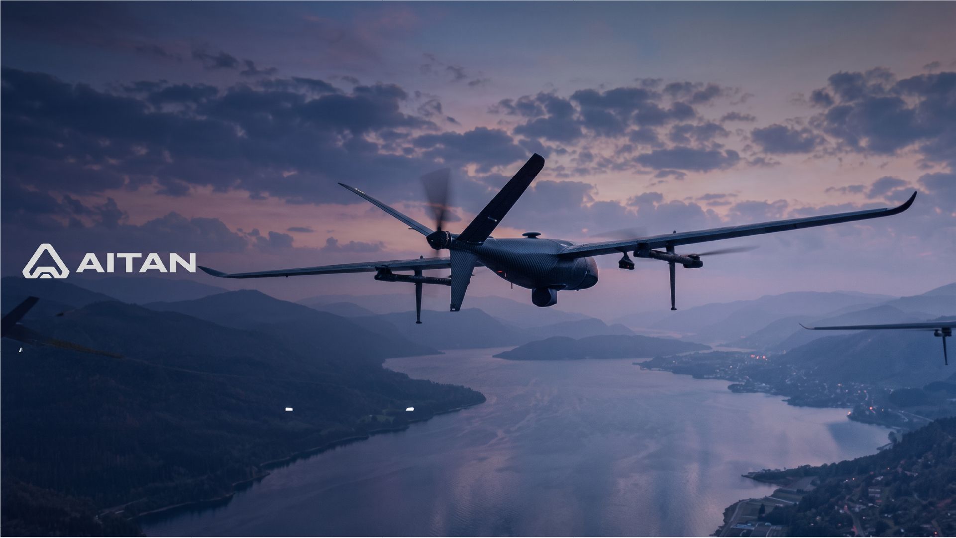 Aitan military drone flying over a mountainous landscape and lake at dusk, with the Aitan logo displayed on the left.