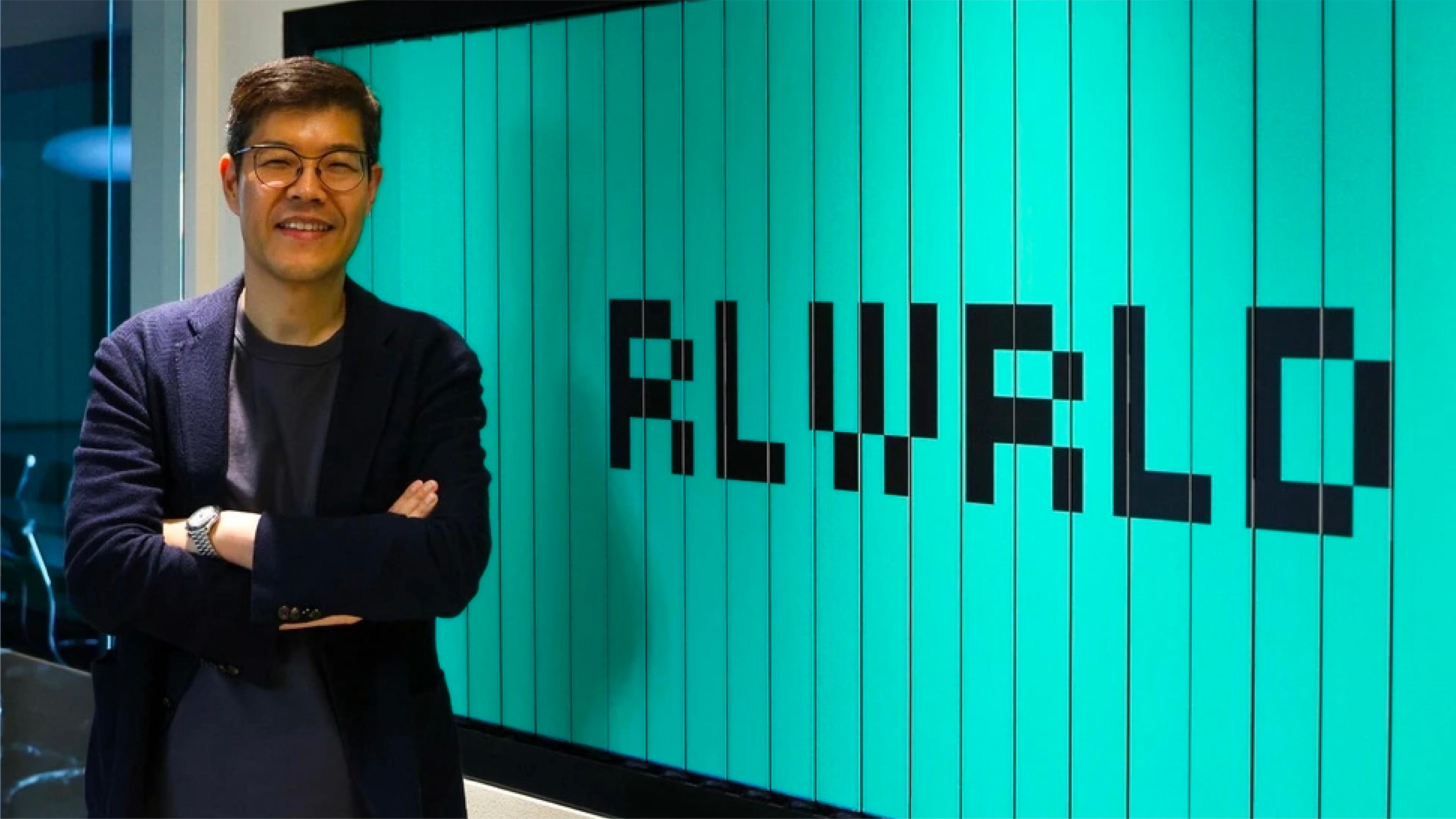 RLWRLD founder and CEO Junghee Ryu stands beside a large RLWRLD logo display.