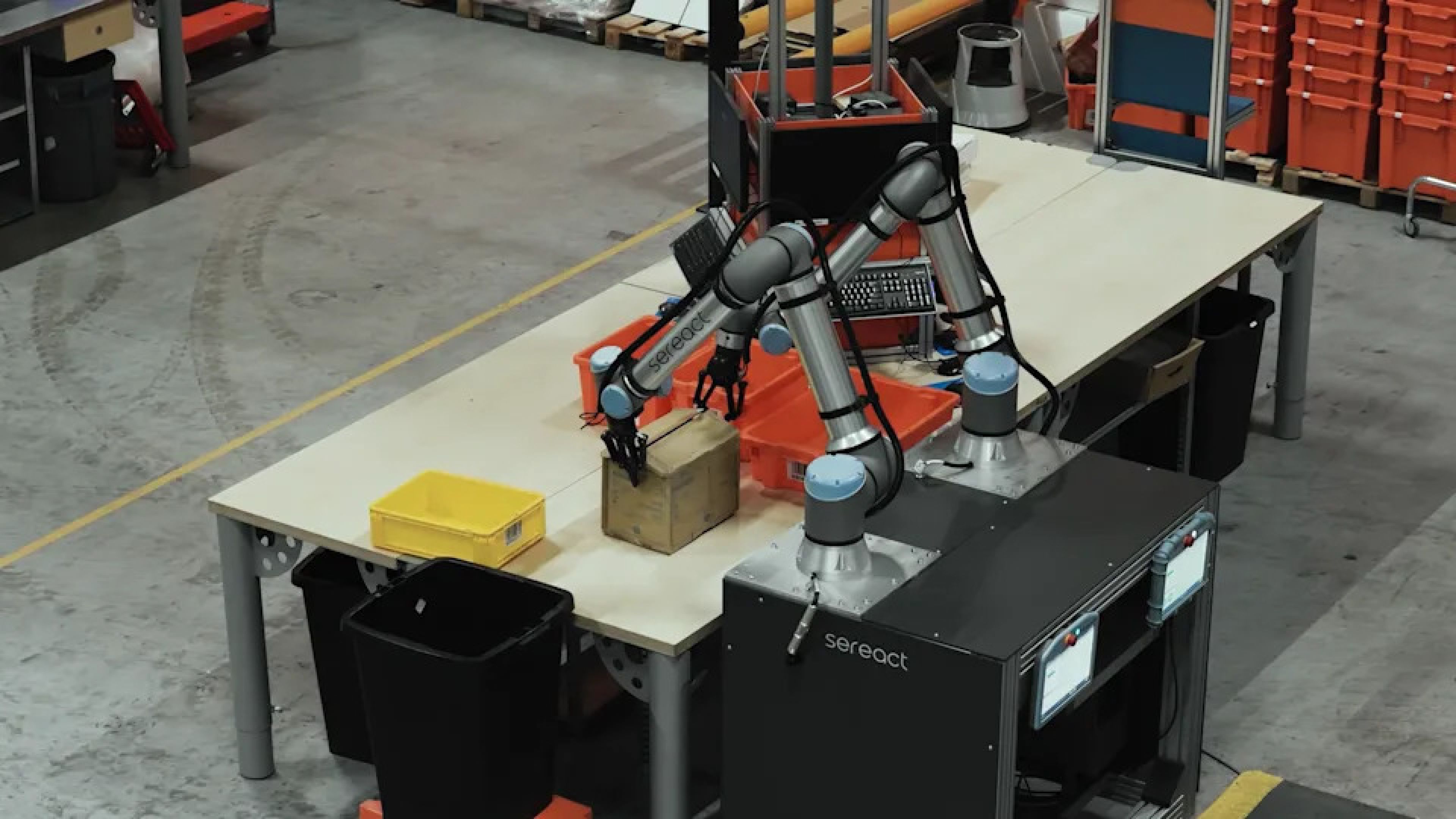 A Sereact dual-arm robotic system uses grippers to handle a cardboard package at a warehouse.