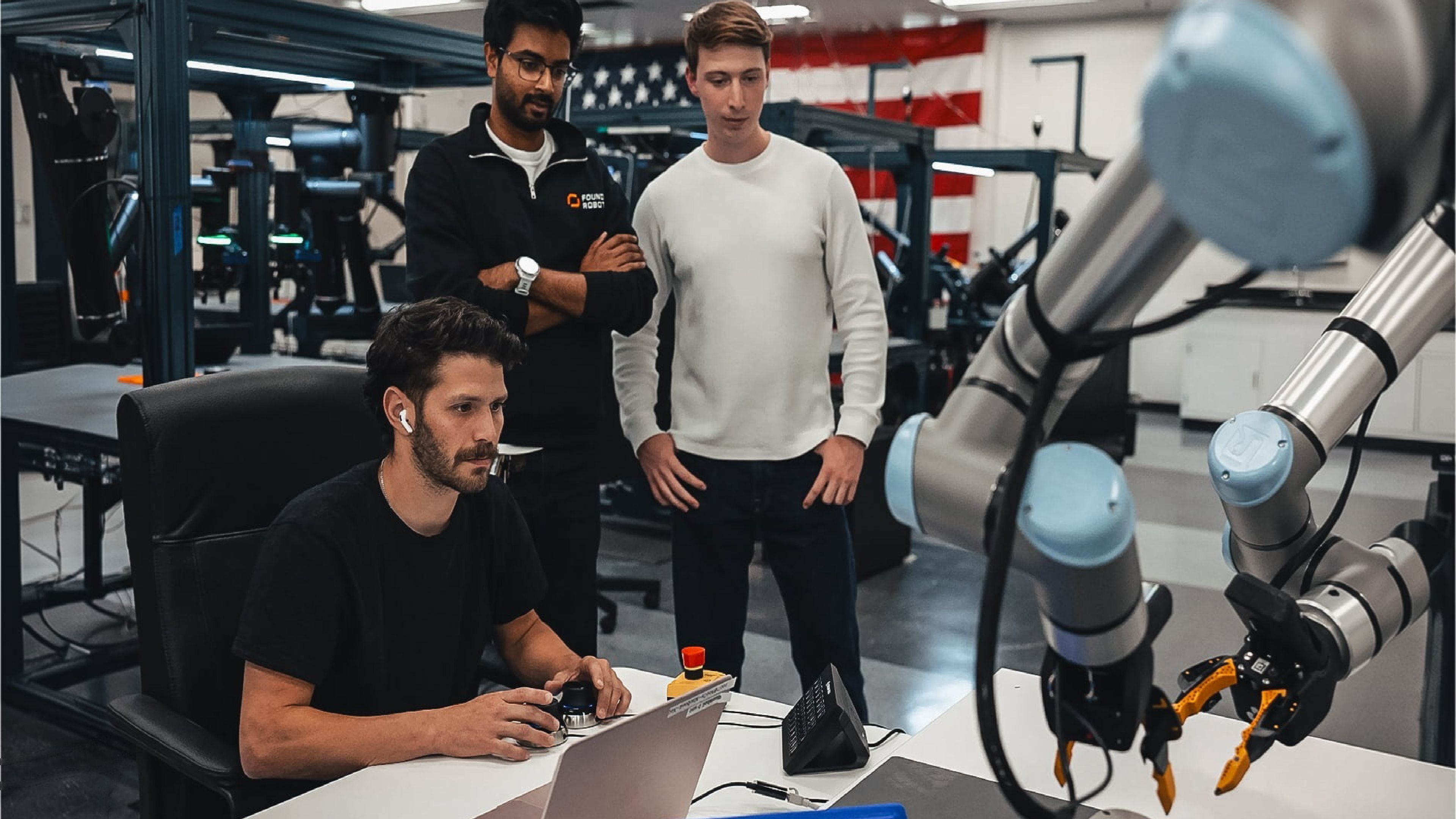 Foundry Robotics team members monitor a dual-arm robotic assembly system at a workstation inside a manufacturing facility.