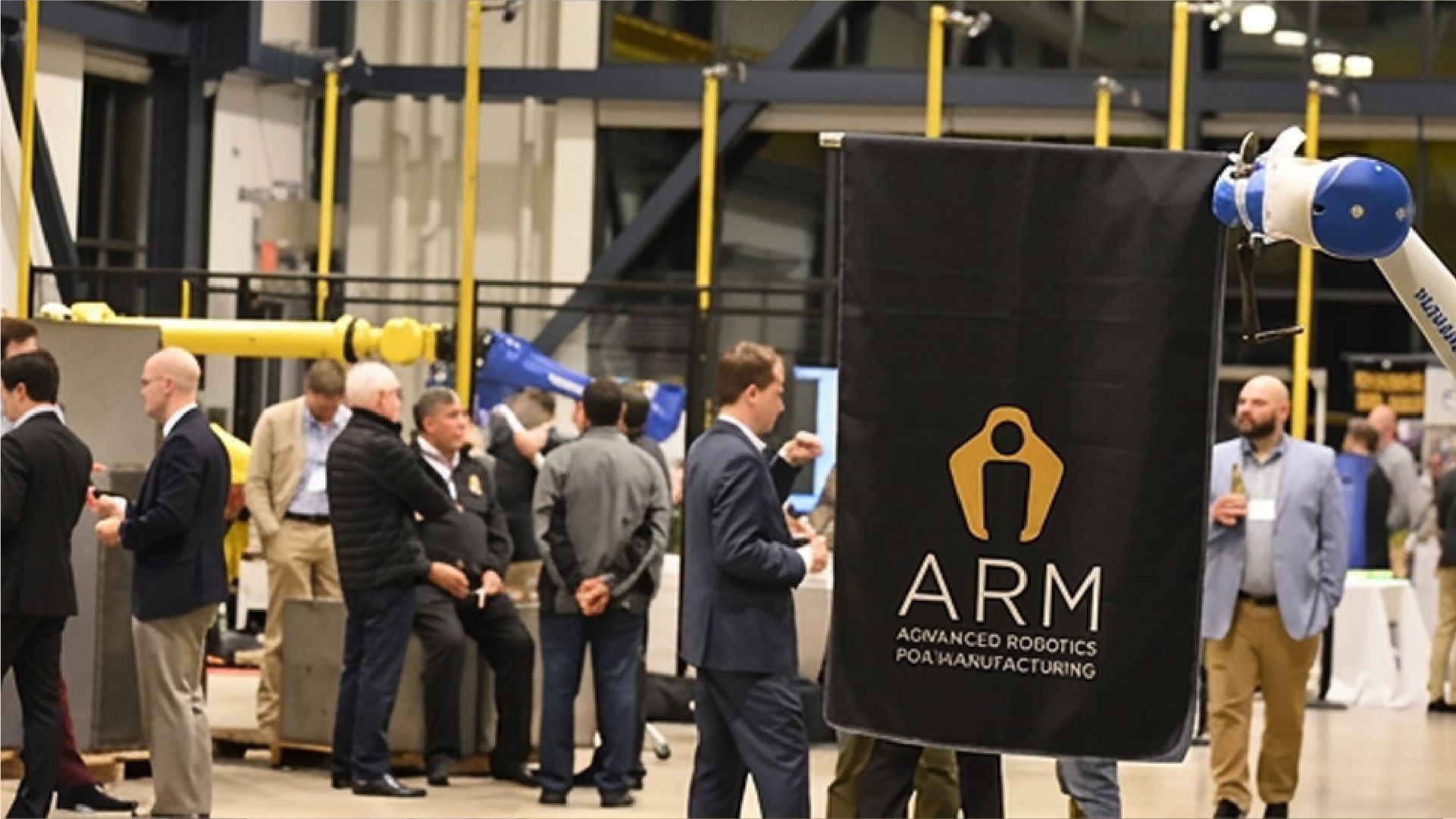 ARM Institute event featuring industrial robotic arms and attendees gathered around an Advanced Robotics for Manufacturing display.
