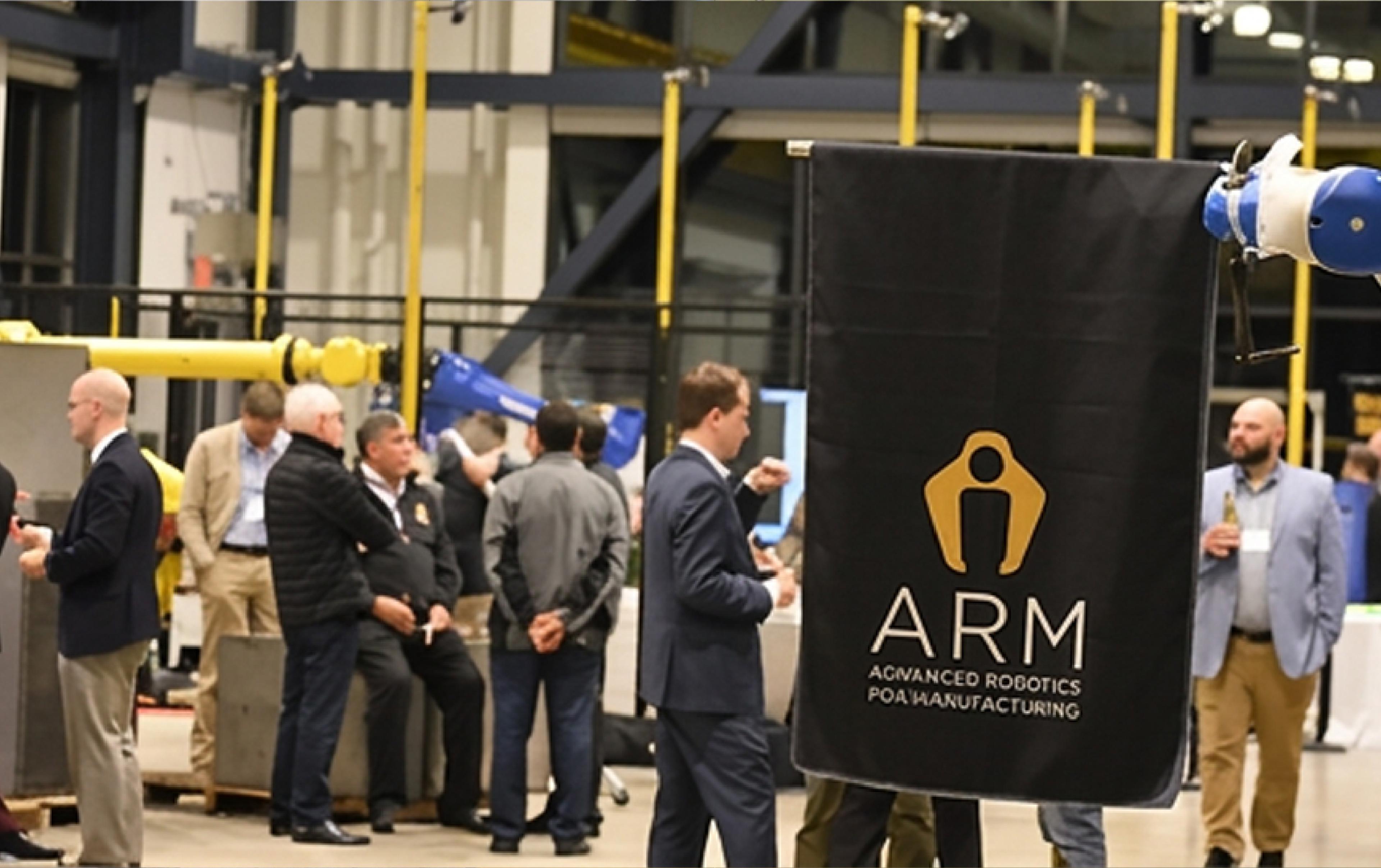 ARM Institute event featuring industrial robotic arms and attendees gathered around an Advanced Robotics for Manufacturing display.
