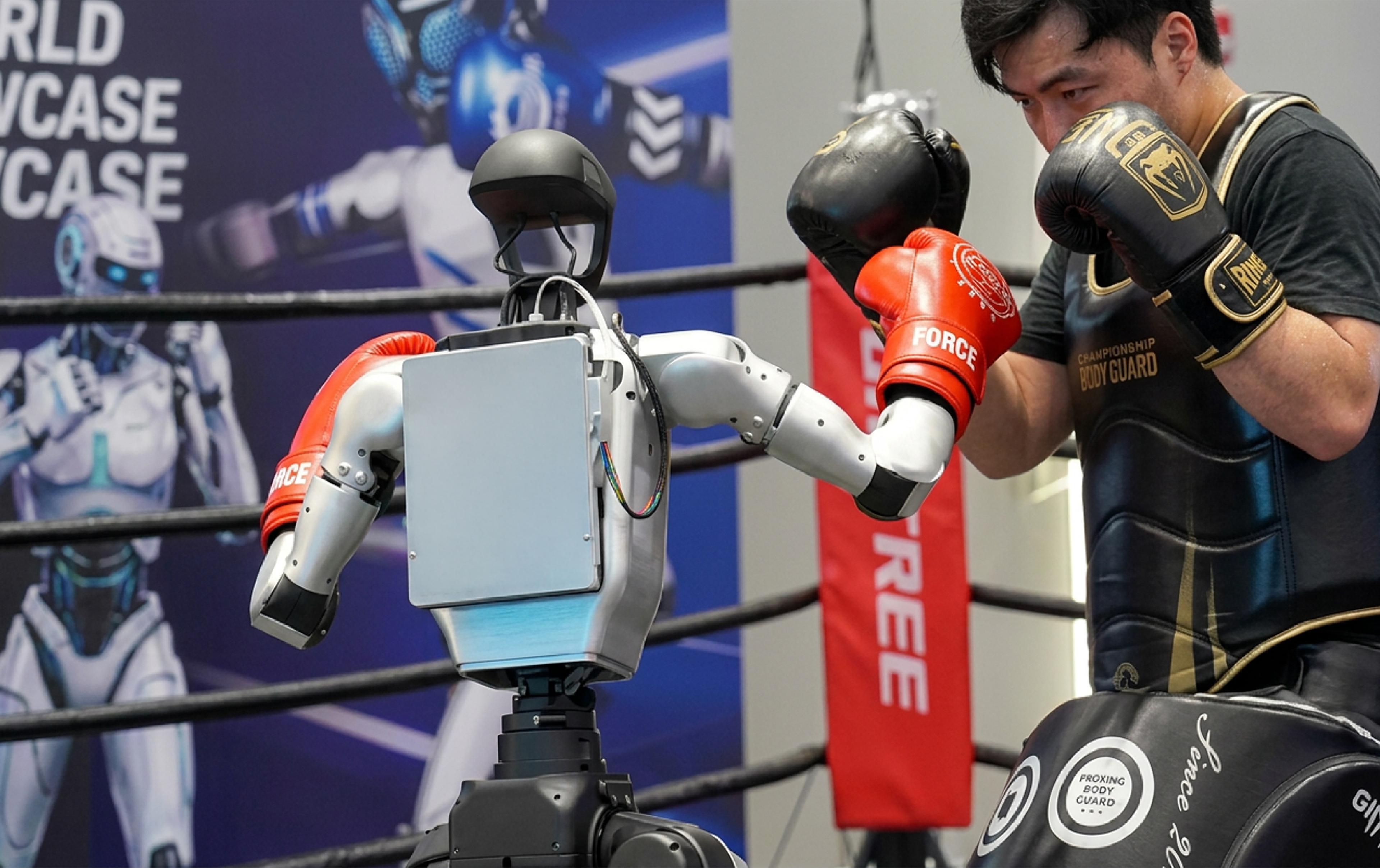 Unitree humanoid robot wearing red boxing gloves faces a human boxer in protective gear inside a boxing ring.