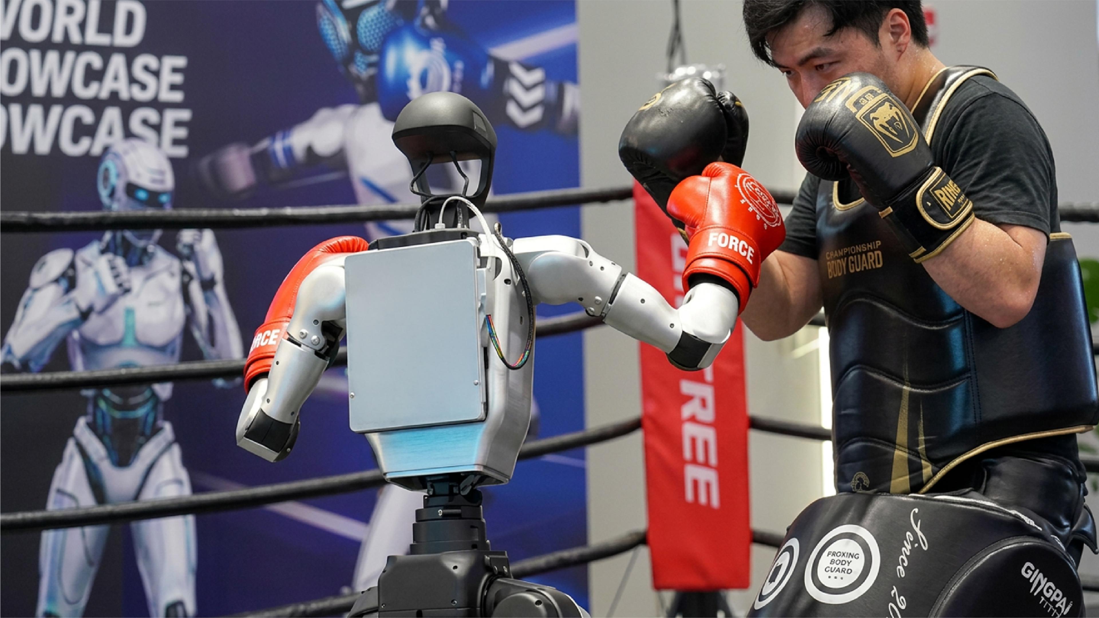 Unitree humanoid robot wearing red boxing gloves faces a human boxer in protective gear inside a boxing ring.