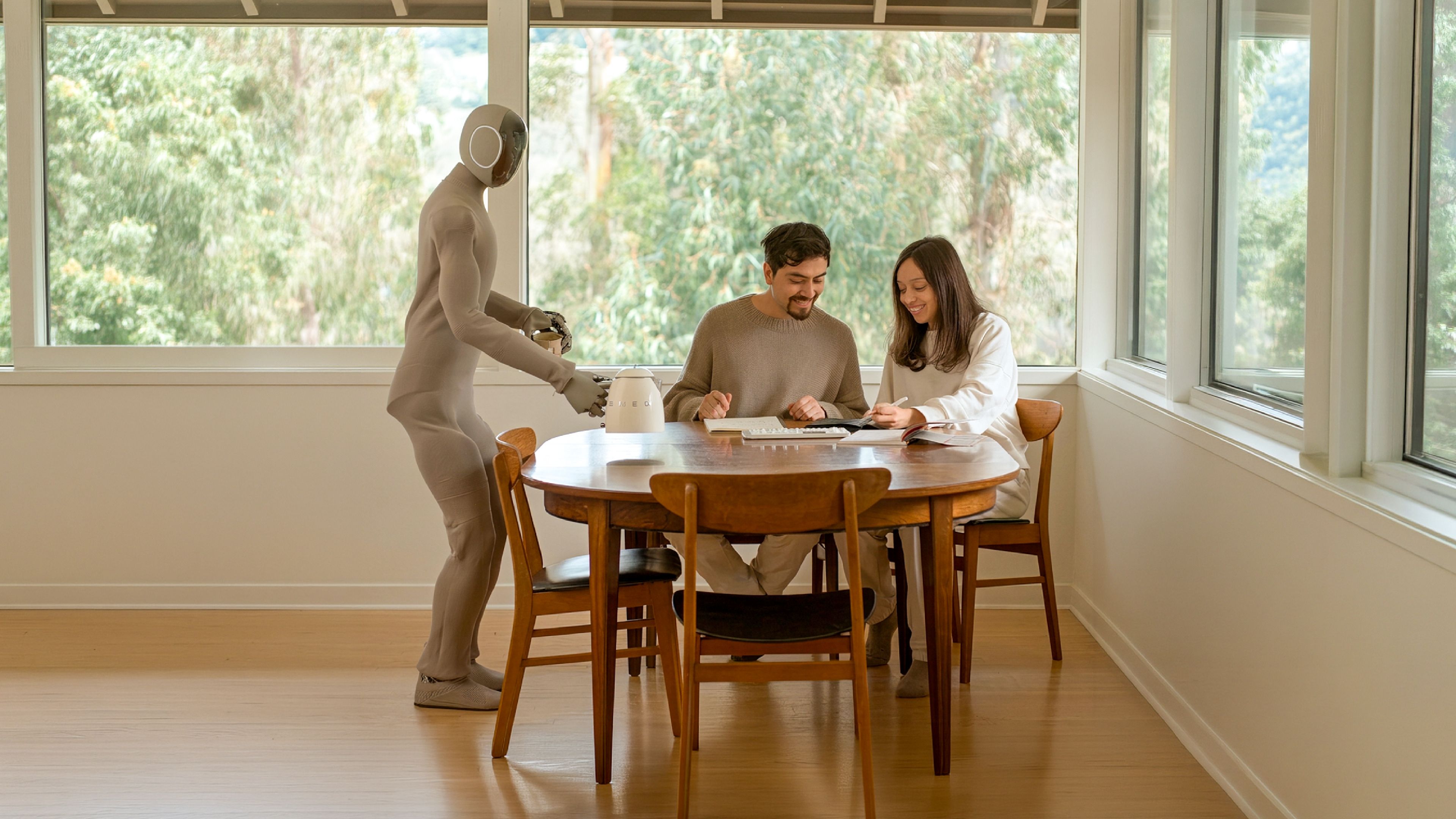 A humanoid home robot pours a drink for two people working at a dining table