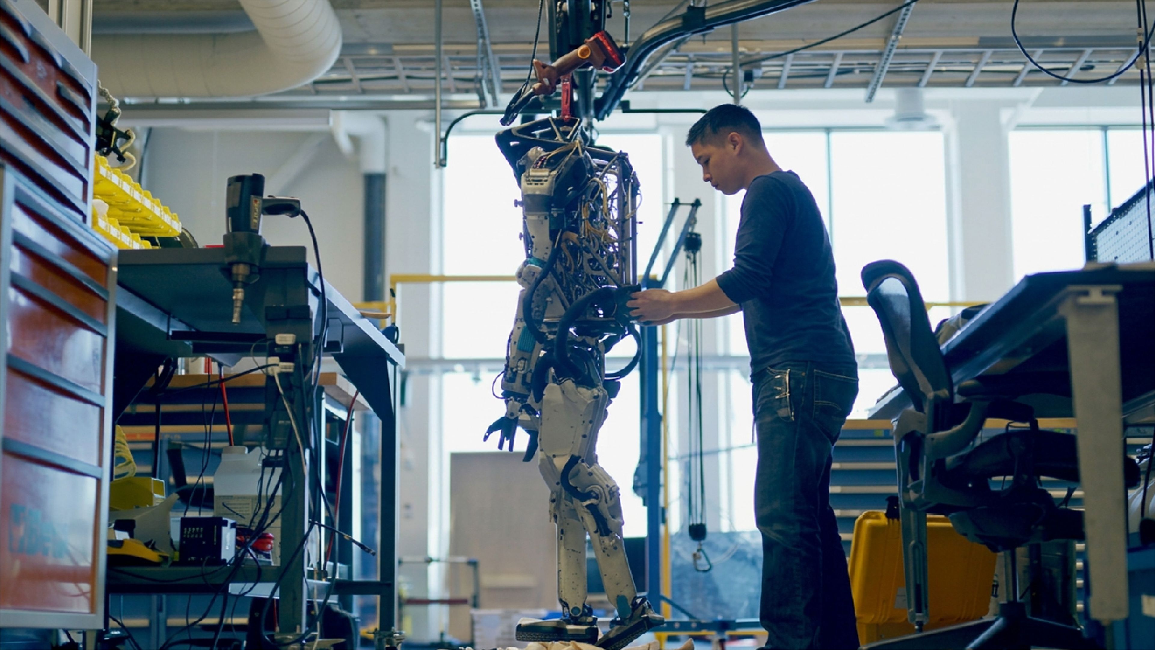 An engineer works on a suspended humanoid robot prototype at a Boston Dynamics robotics laboratory.