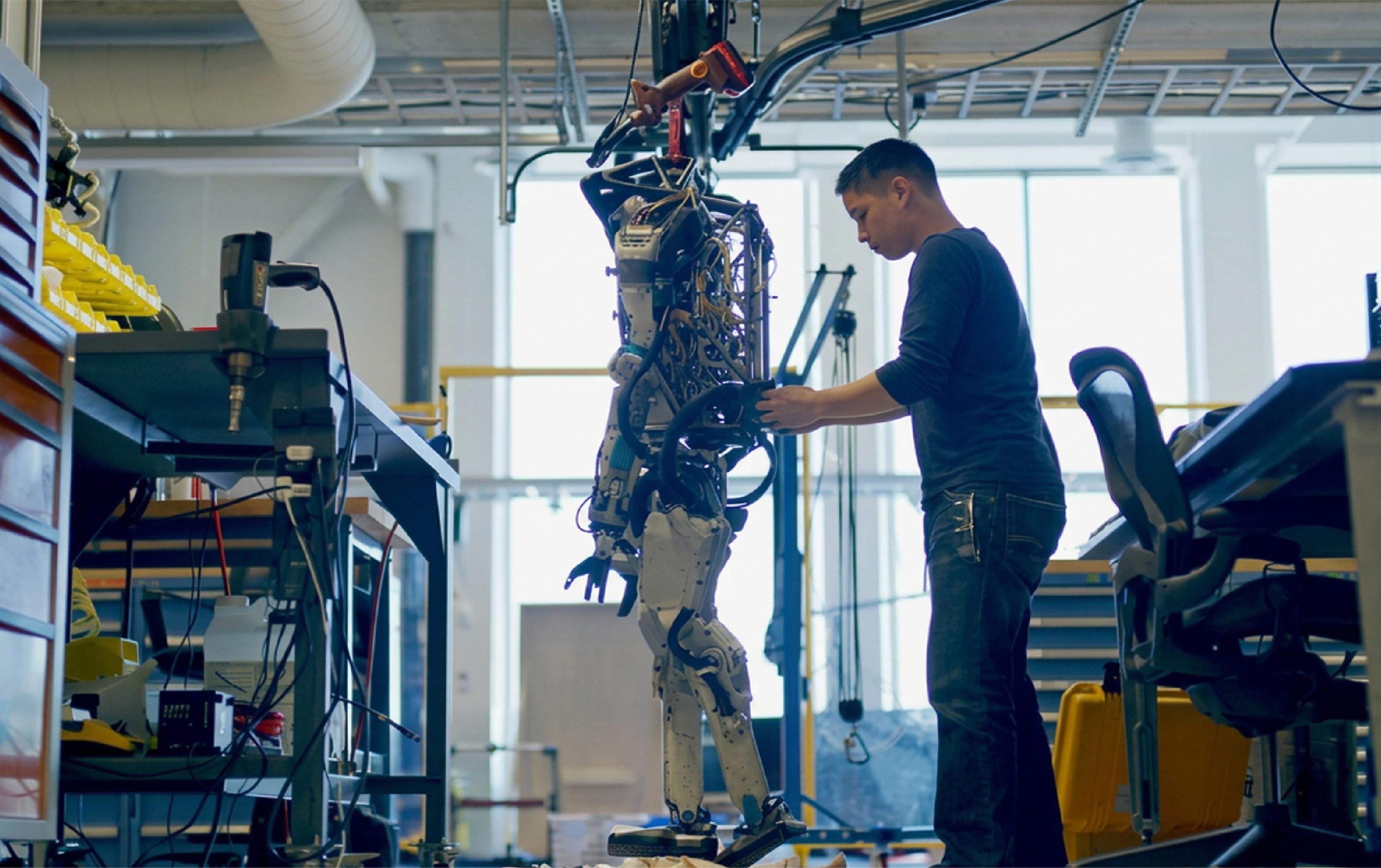An engineer works on a suspended humanoid robot prototype at a Boston Dynamics robotics laboratory.