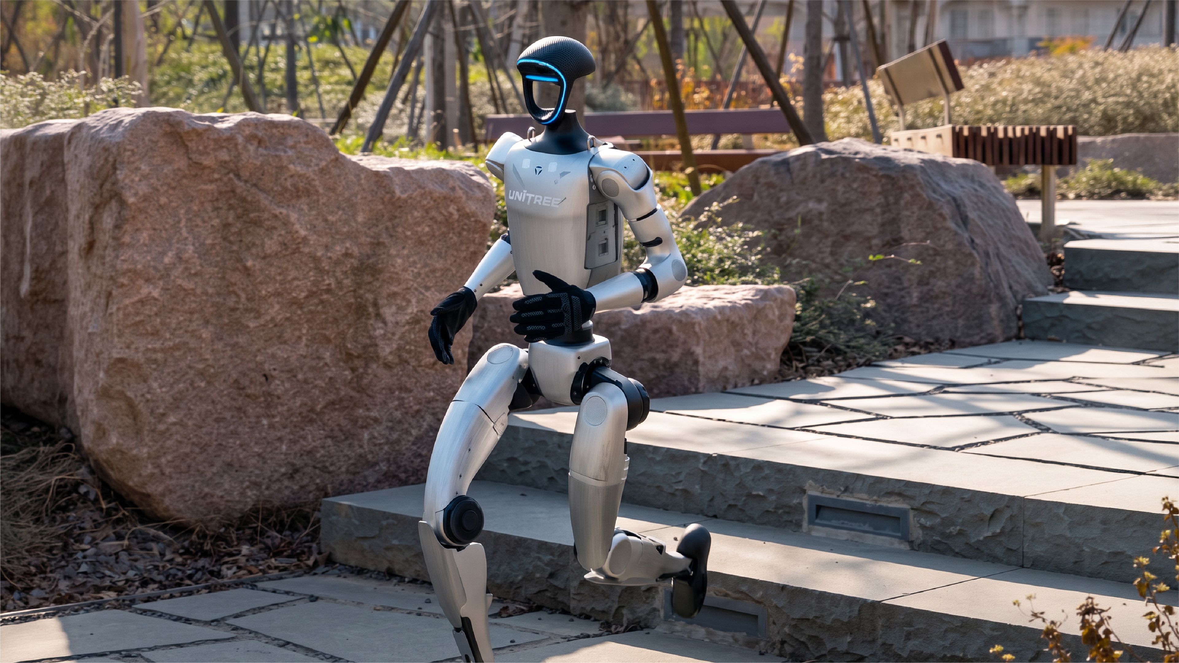 A Unitree humanoid robot walks down stone steps in an outdoor park.