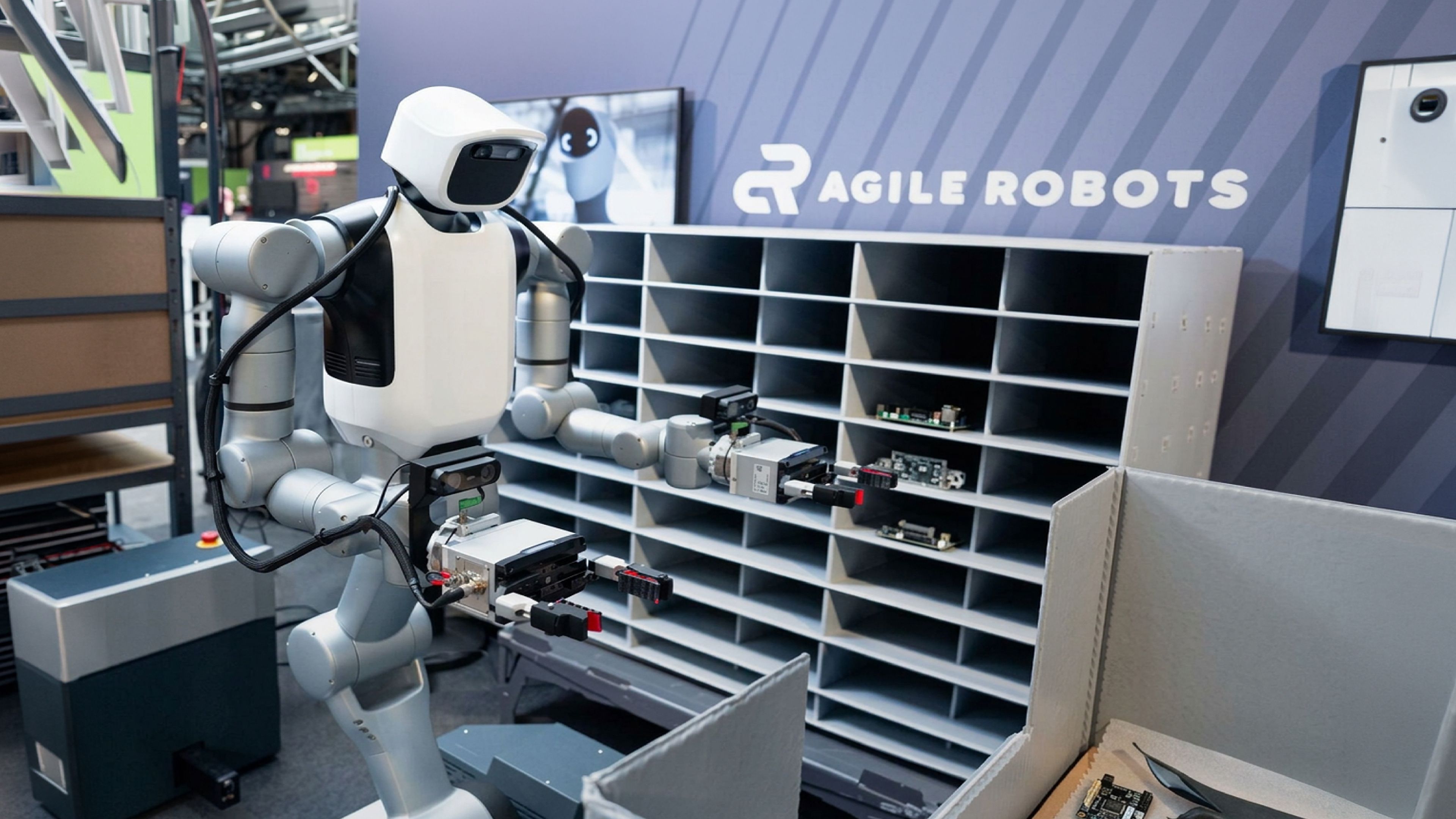 Agile Robots' dual-arm mobile humanoid handles electronic components in front of a parts storage rack.