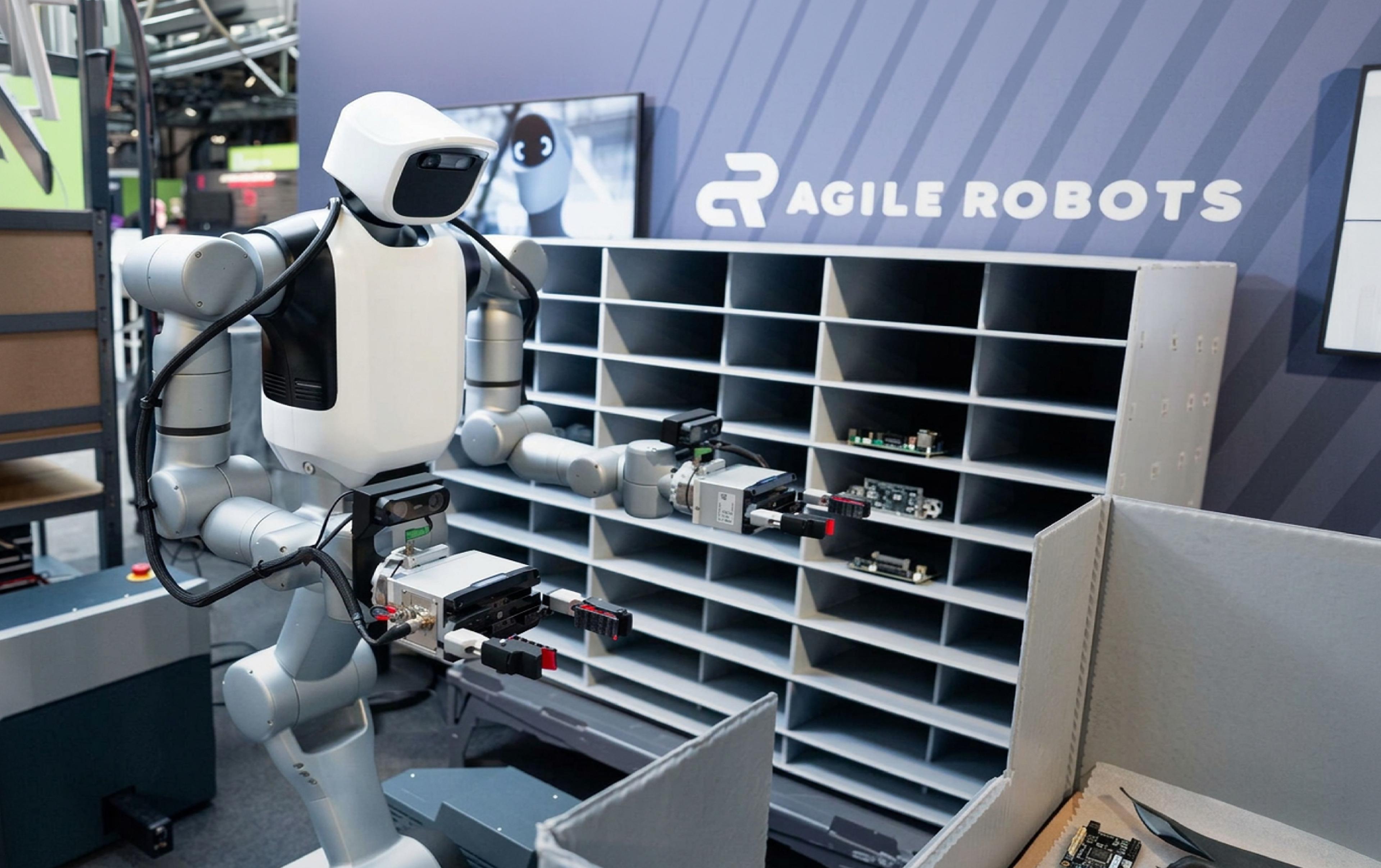 Agile Robots' dual-arm mobile humanoid handles electronic components in front of a parts storage rack.
