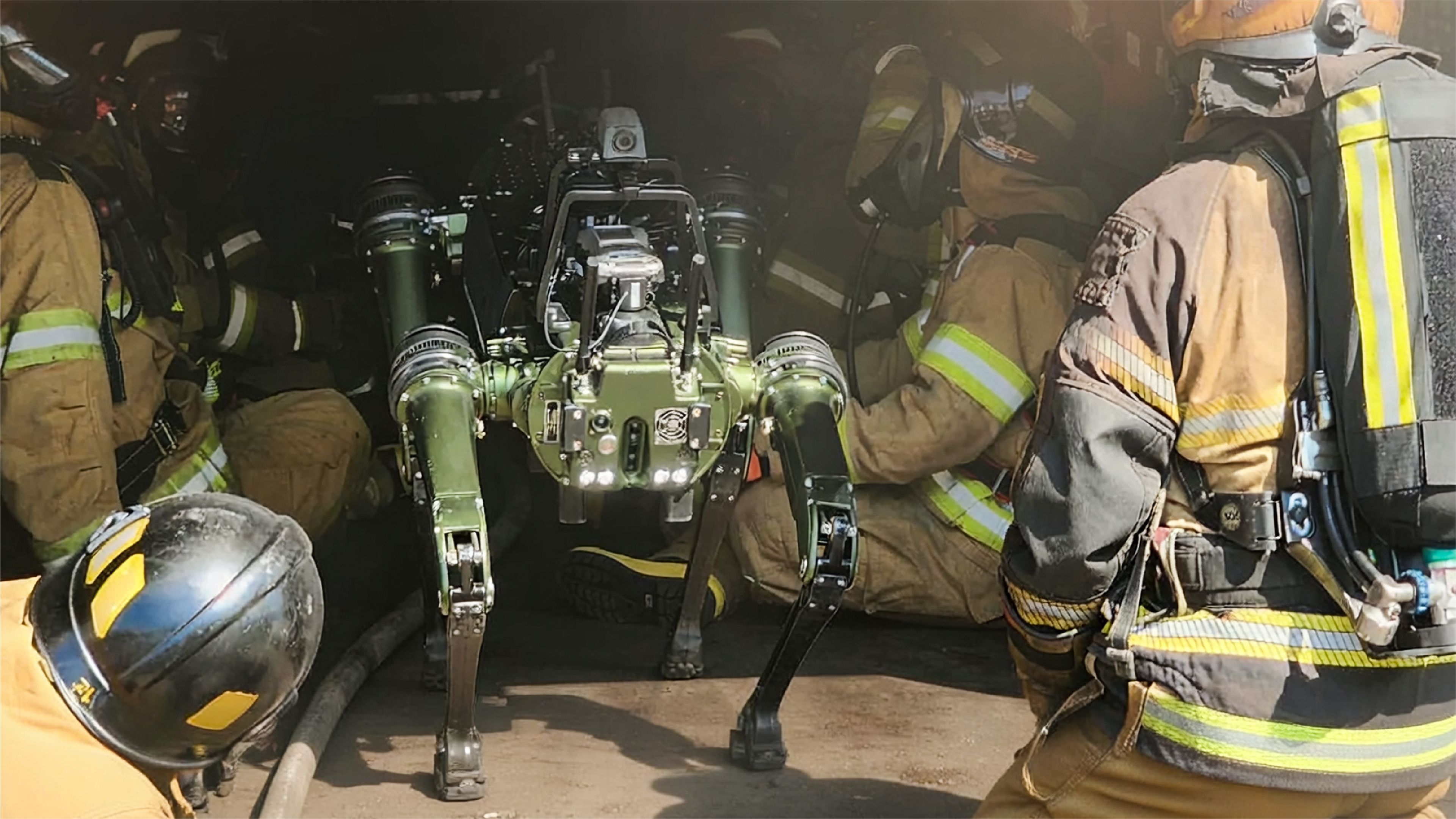 A quadruped robot stands among firefighters during an emergency response training exercise inside a dark, smoke-filled structure.