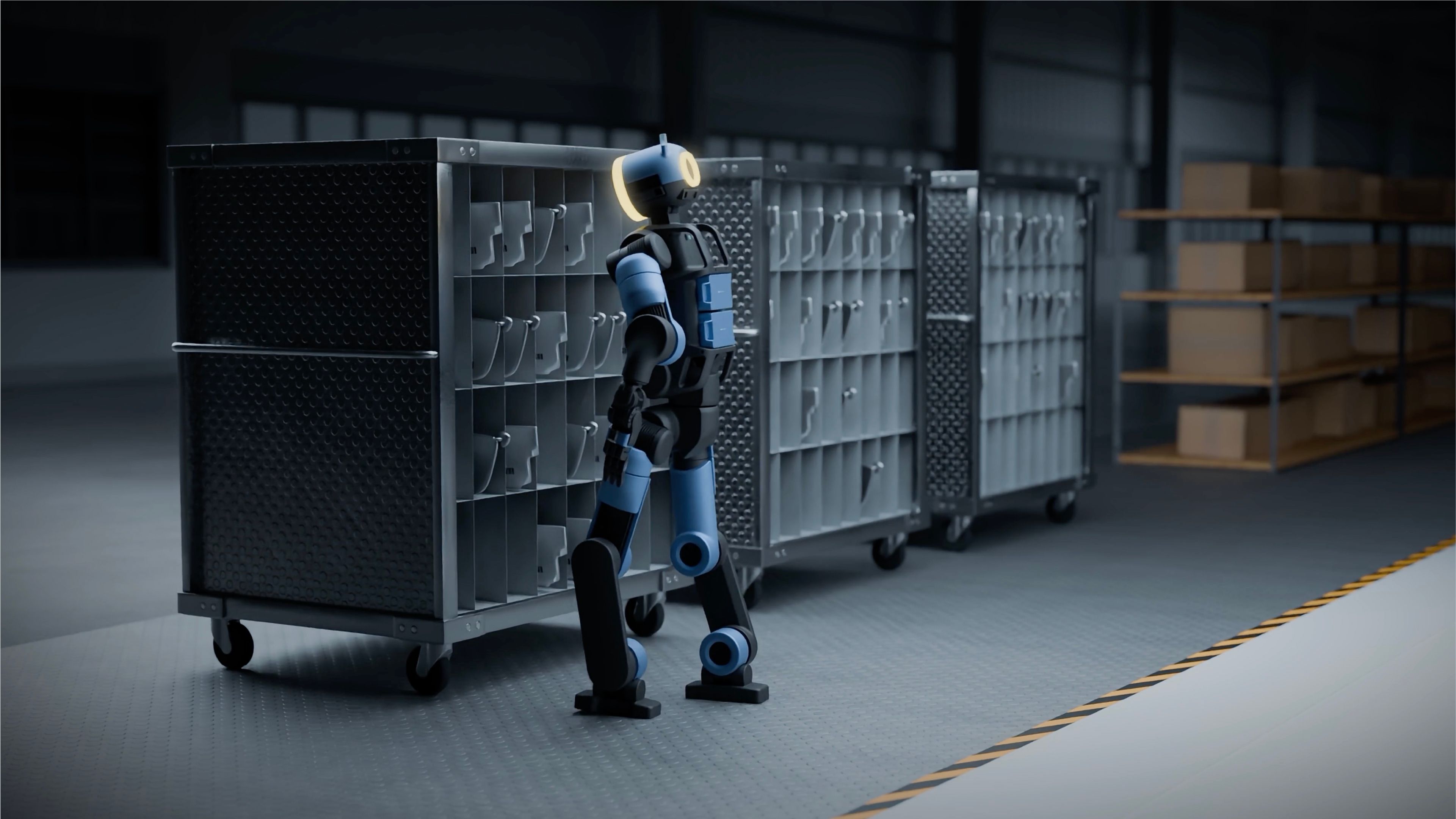 A bipedal humanoid robot stands in profile facing a line of metal parts carts in a dimly lit industrial warehouse.