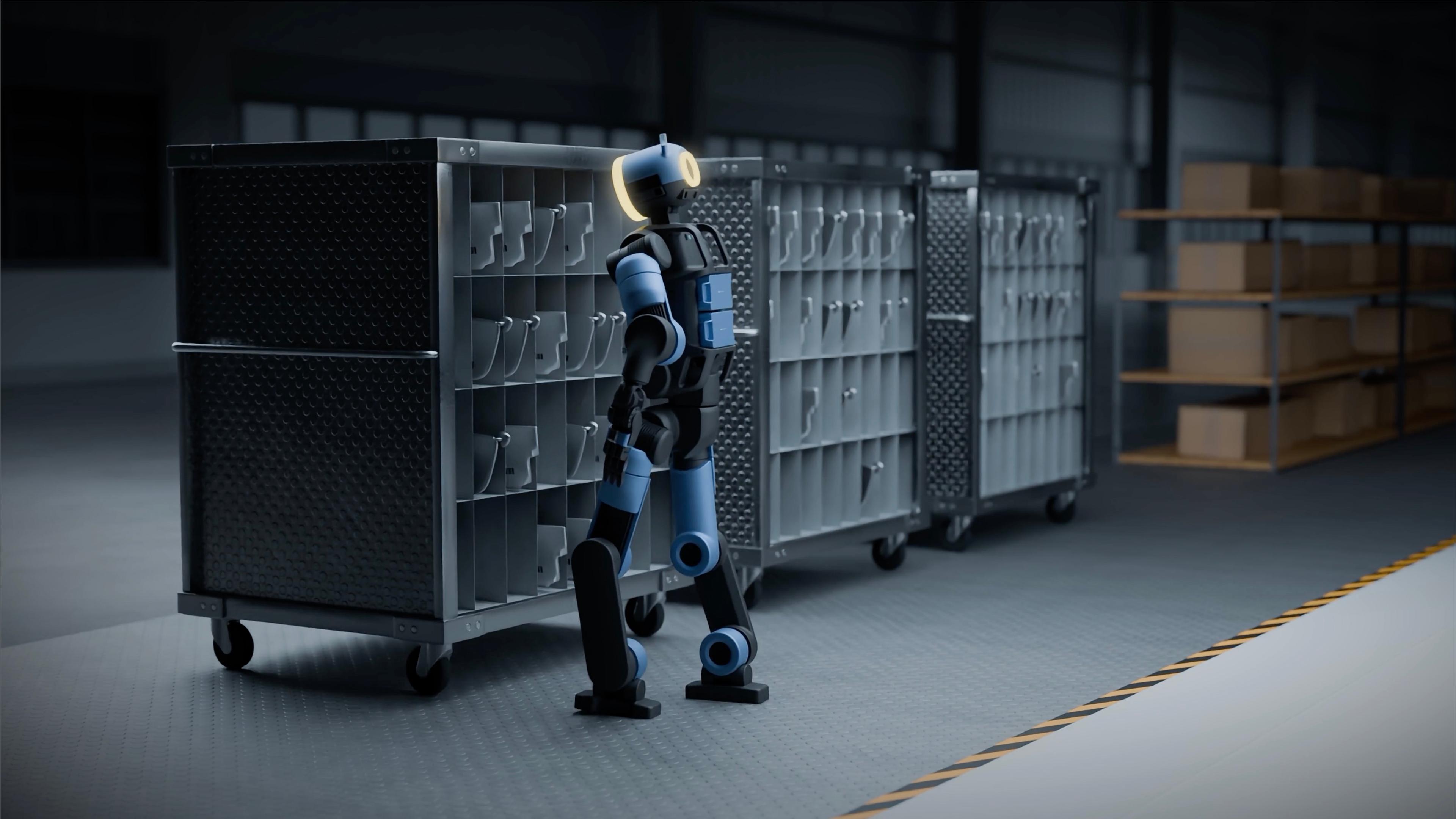 A bipedal humanoid robot stands in profile facing a line of metal parts carts in a dimly lit industrial warehouse.