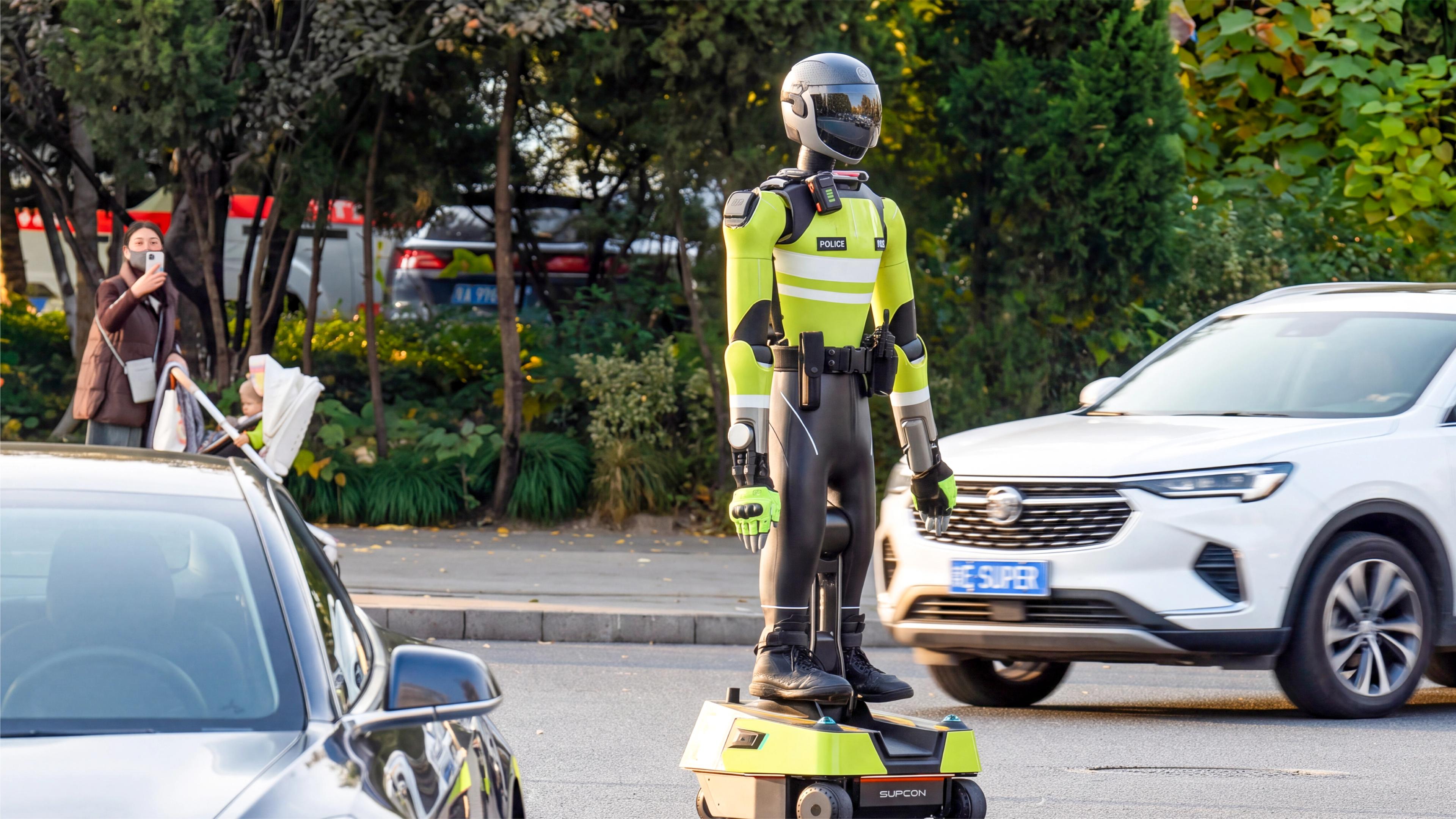 A humanoid robot dressed in a police uniform and helmet stands balanced on a wheeled mobility base