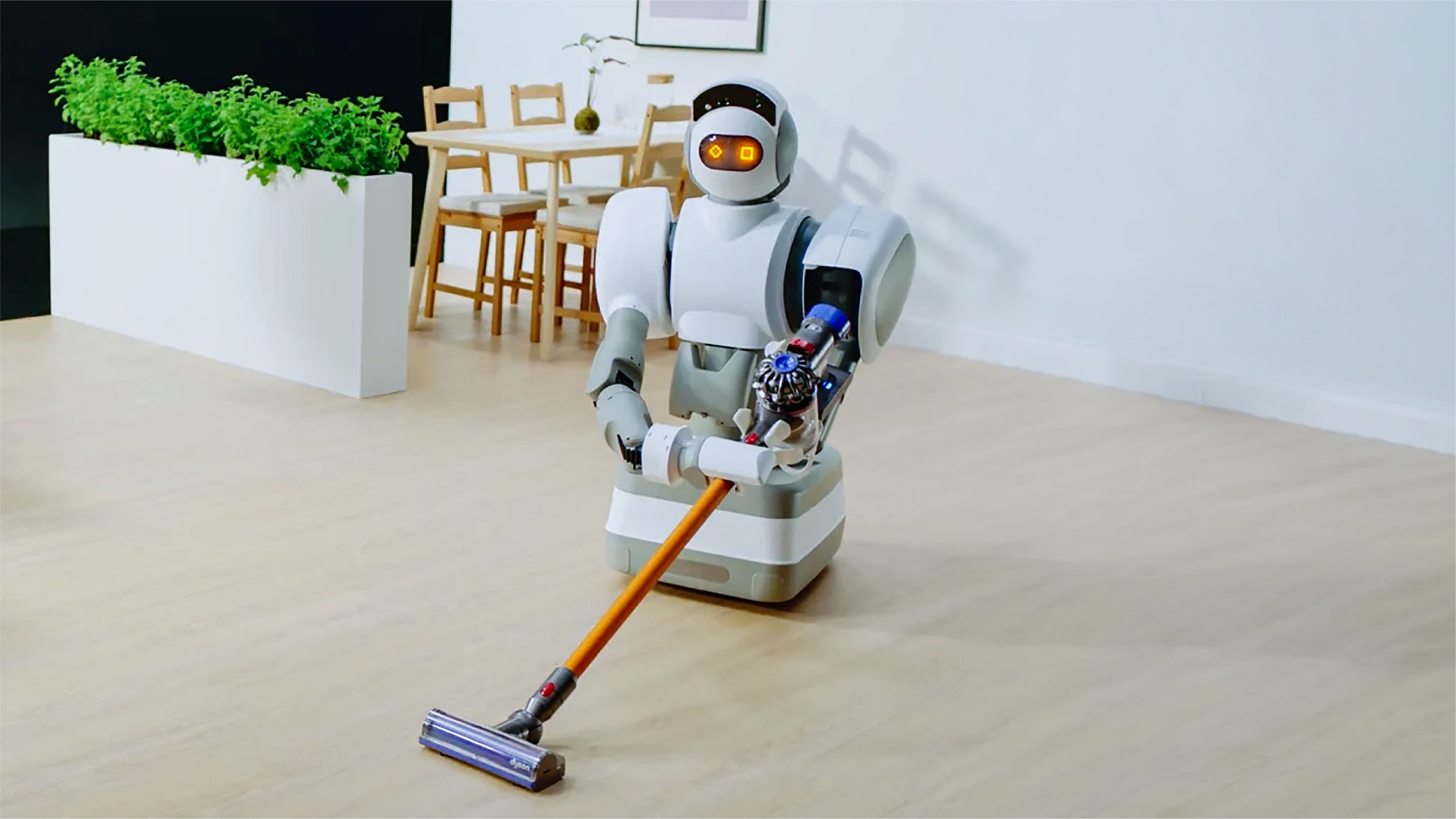 Humanoid robot with glowing orange eyes and a wheeled base pushing a cordless vacuum across a wooden floor in a dining room