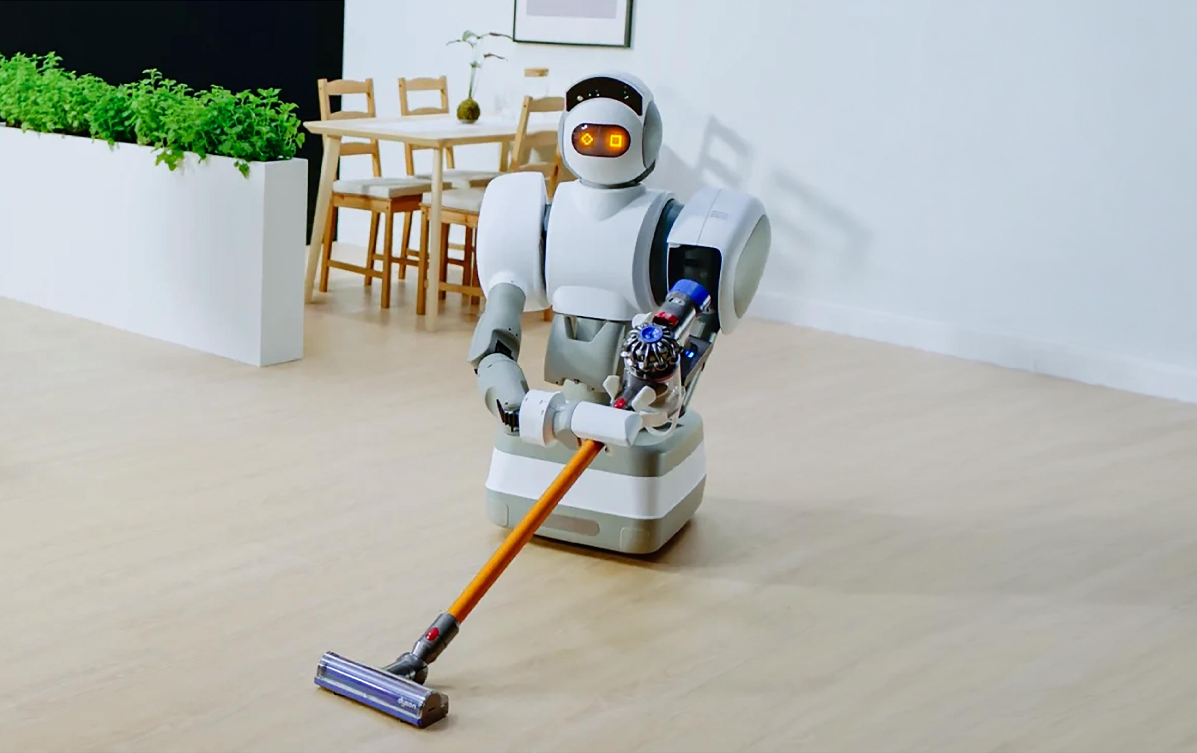 Humanoid robot with glowing orange eyes and a wheeled base pushing a cordless vacuum across a wooden floor in a dining room