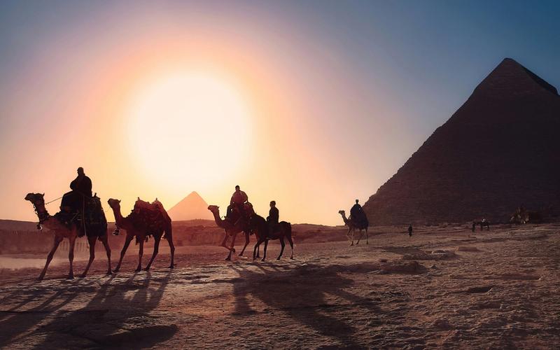 People ride camels in front of the  pyramids