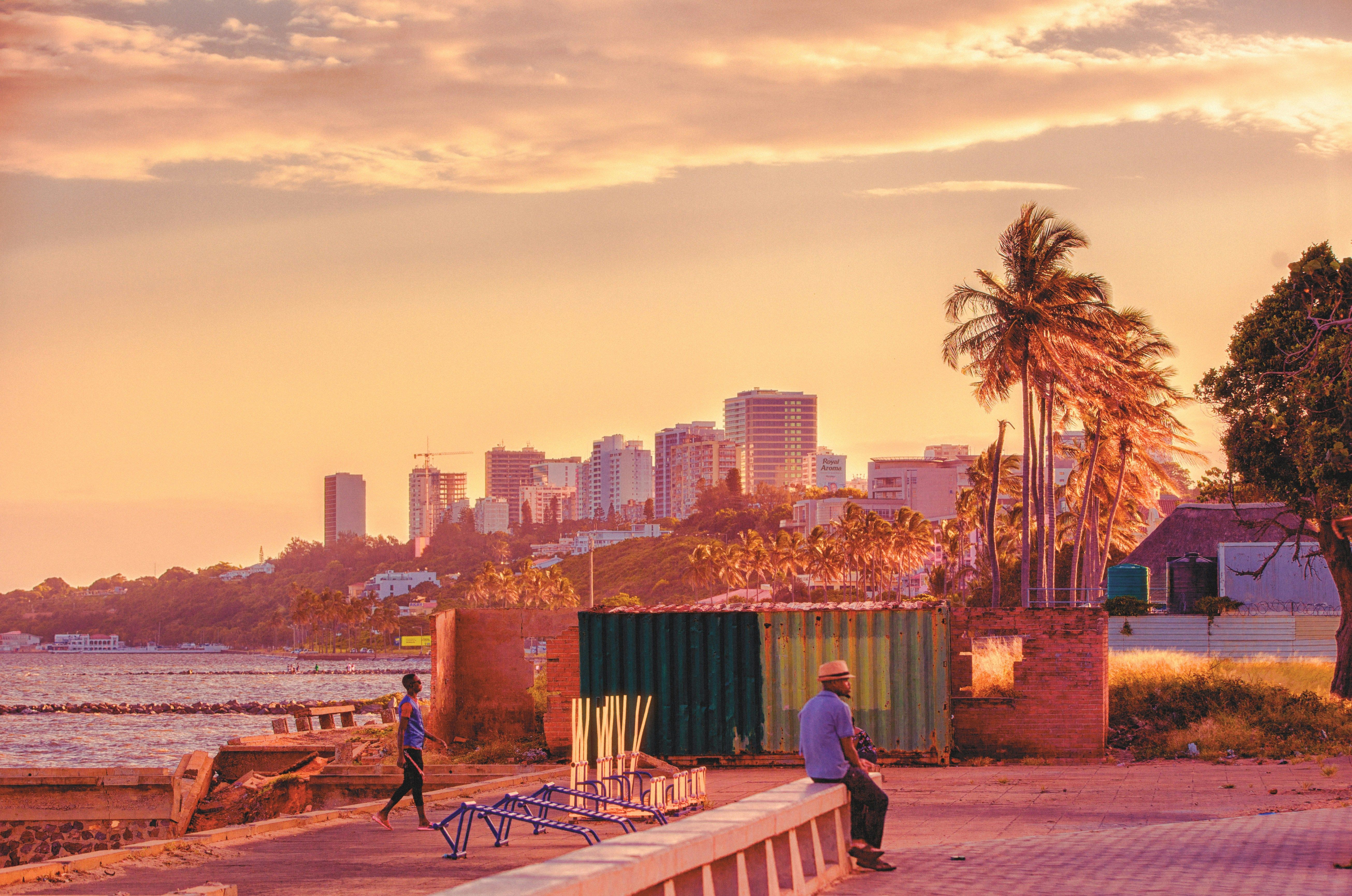 A man sitting on a wall with buildings and the sea in the background in Maputo, Mozambique