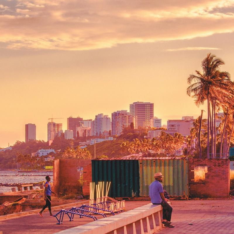 A man sitting on a wall with buildings and the sea in the background in Maputo, Mozambique