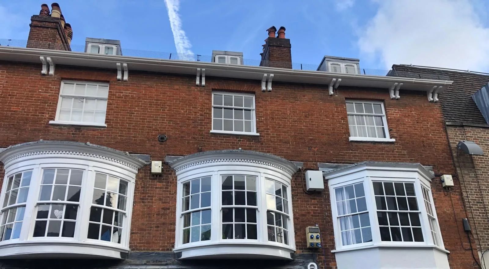 Three renewed white bow sash windows in a red brick Georgian terrace against a blue sky
