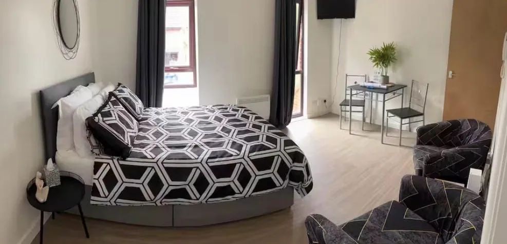 Bright refurbished studio flat with a double bed, tall curtained windows and a small dining table on pale wood flooring