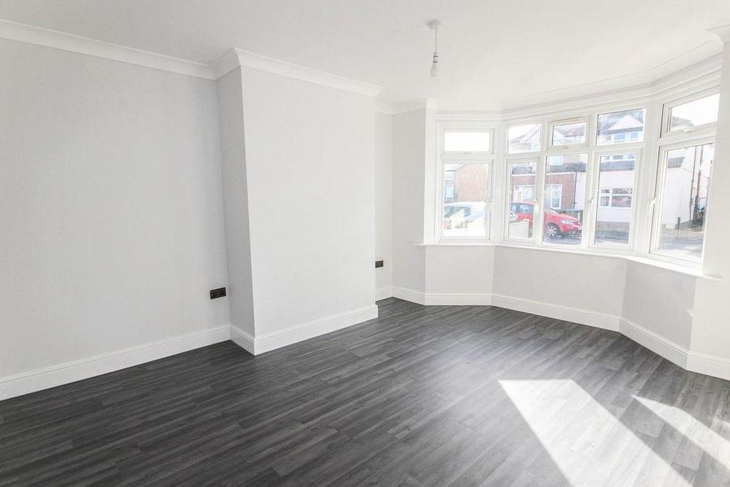 A refurbished living room with a bay window, fresh white walls and dark flooring