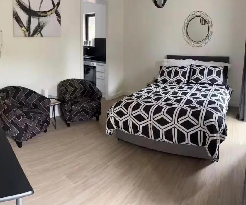 Refurbished studio room with a patterned double bed, two dark tub chairs and a view through to the new kitchen