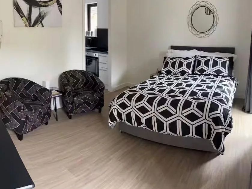 Refurbished studio room with a patterned double bed, two dark tub chairs and a view through to the new kitchen