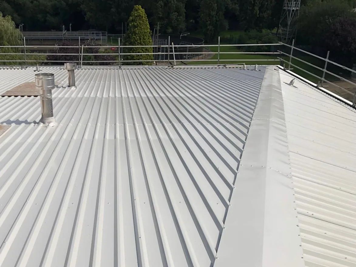 Sunlight across a freshly coated metal roof, with the hip flashing running down towards the eaves