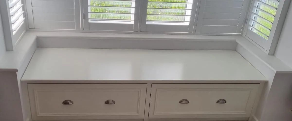 A built-in window seat with two deep drawers below shuttered bay windows