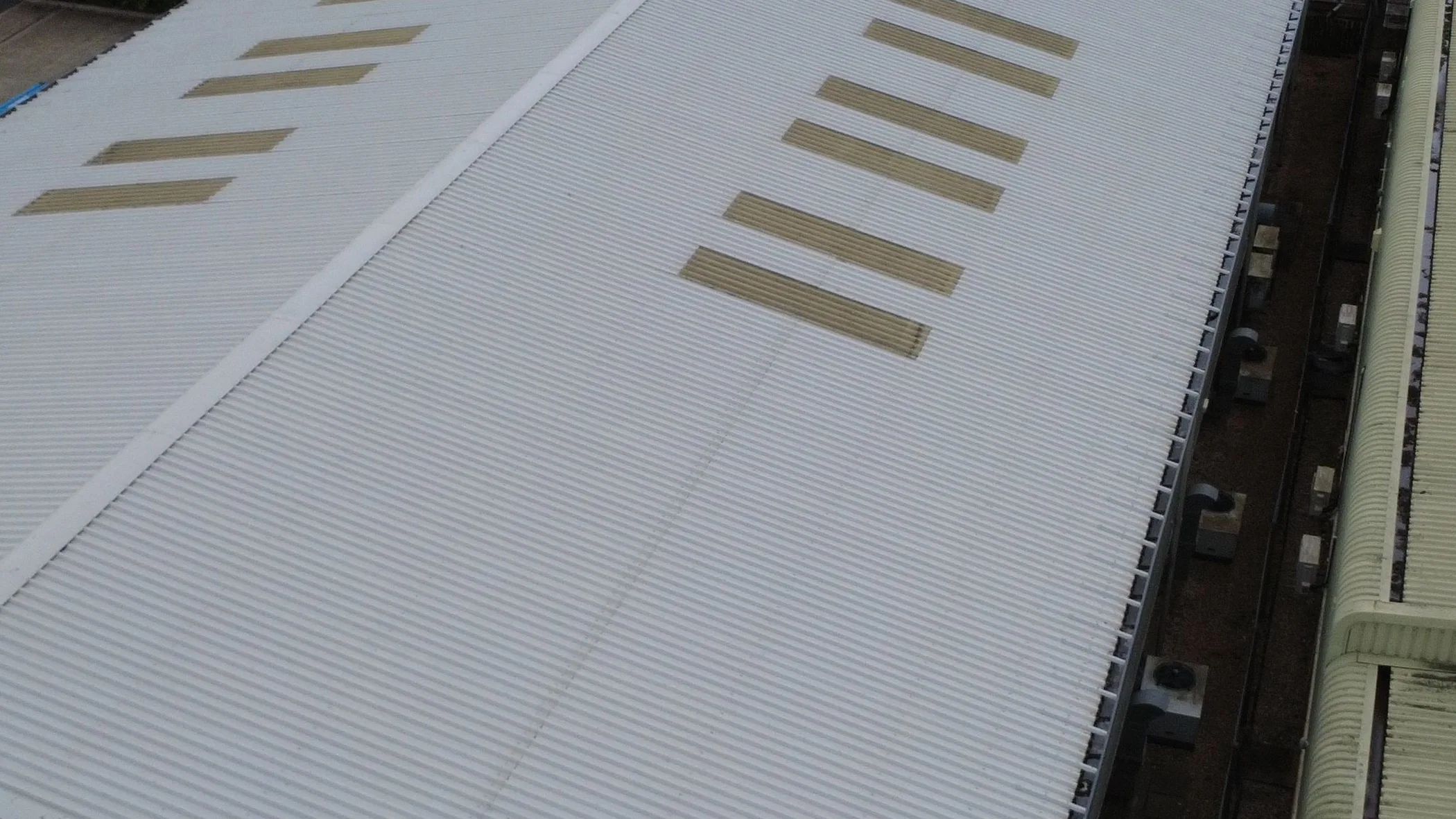 A large industrial roof coated white, its amber rooflights running the length of the building, with an untreated green roof alongside
