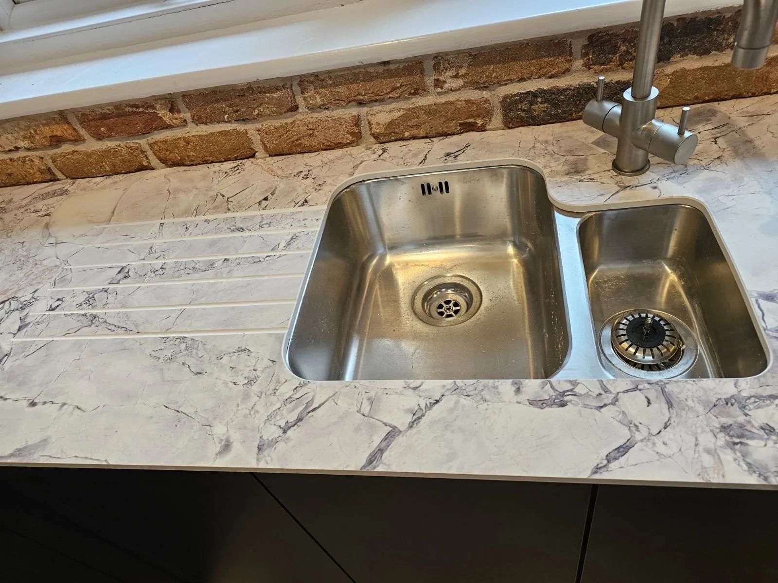 Undermount stainless steel sink with drainer grooves milled into a marble worktop, against reclaimed brick