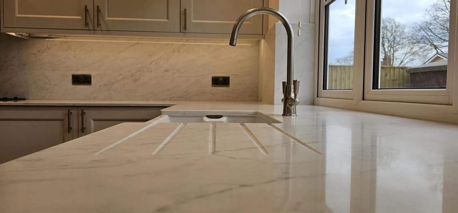 Polished quartz worktop running to an undermount sink and brushed tap, with a garden beyond the window