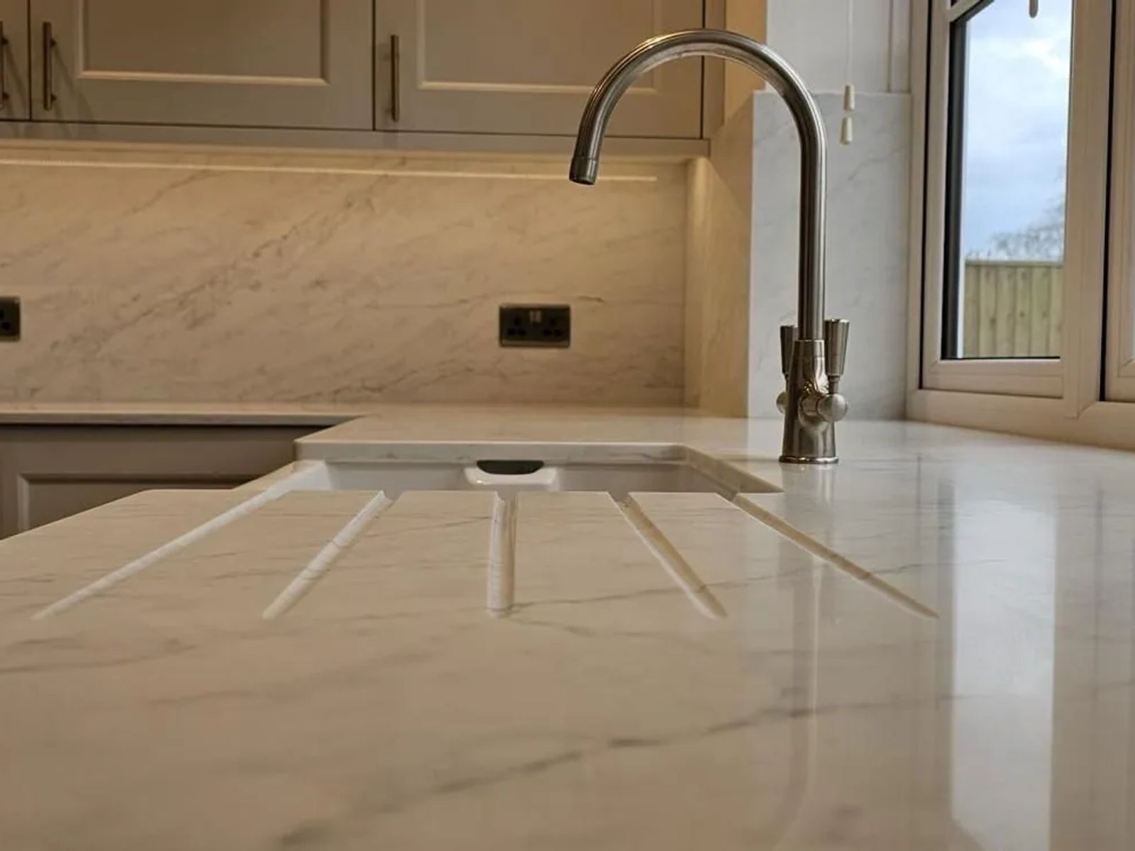 Polished quartz worktop running to an undermount sink and brushed tap, with a garden beyond the window