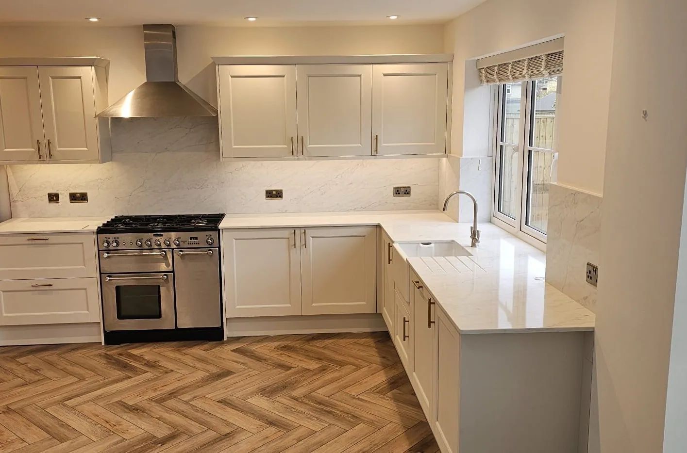 Cream shaker kitchen with brass handles, a marble worktop and oak herringbone flooring
