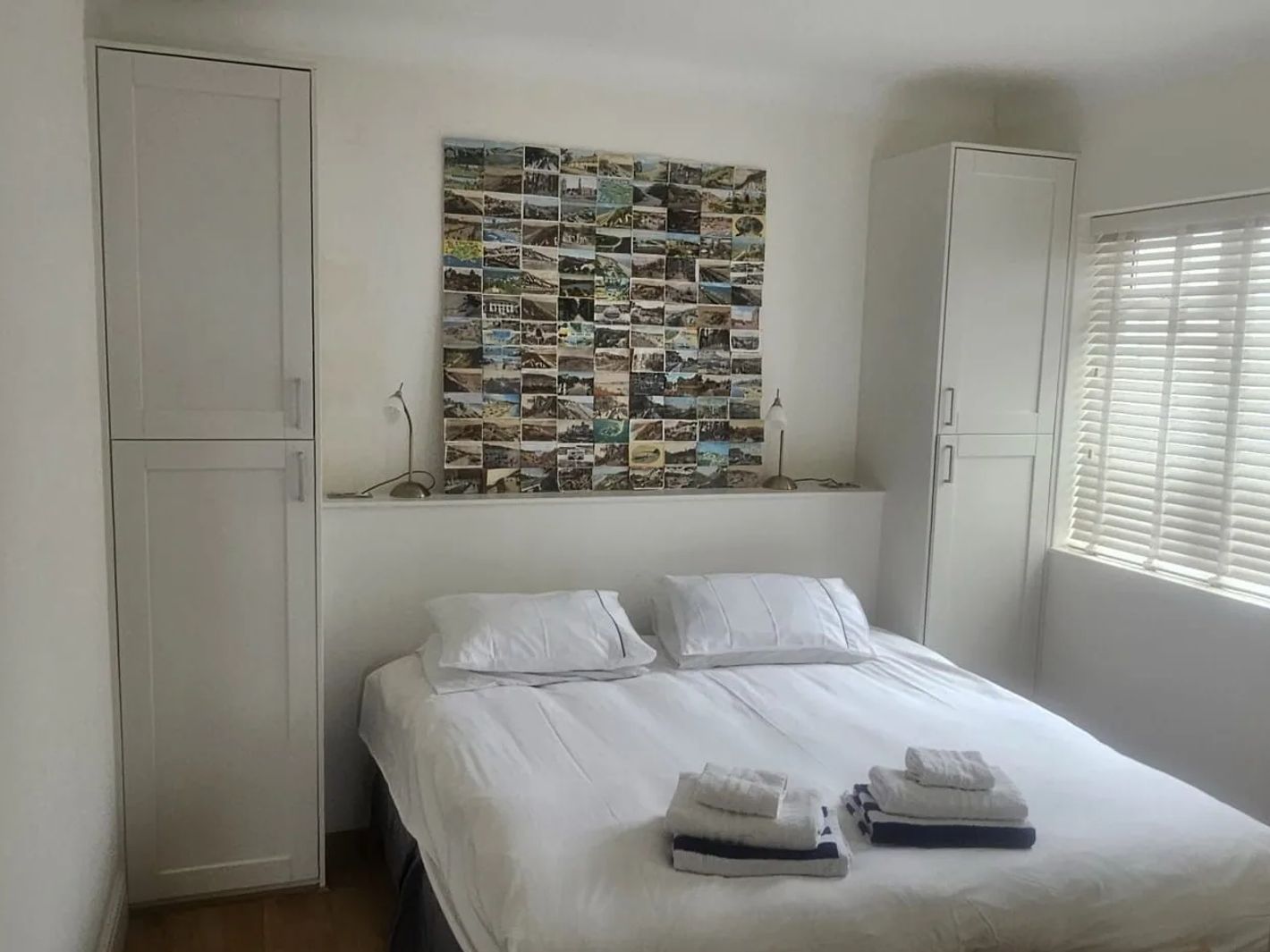 A white bedroom with fitted wardrobes either side of the bed and slatted blinds at the window