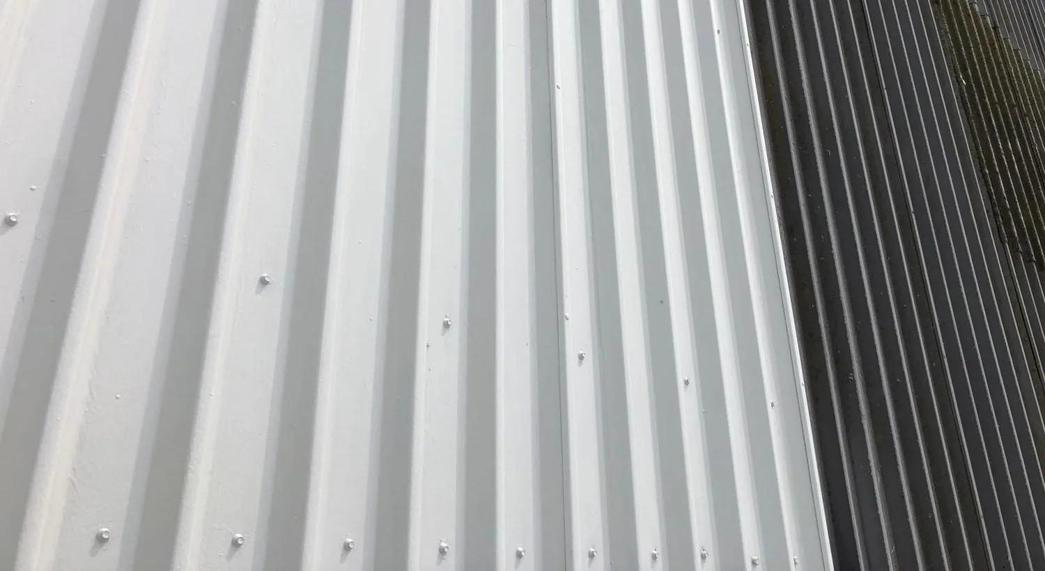 Half a metal roof coated white, the untreated sheets alongside still dark and weather-stained