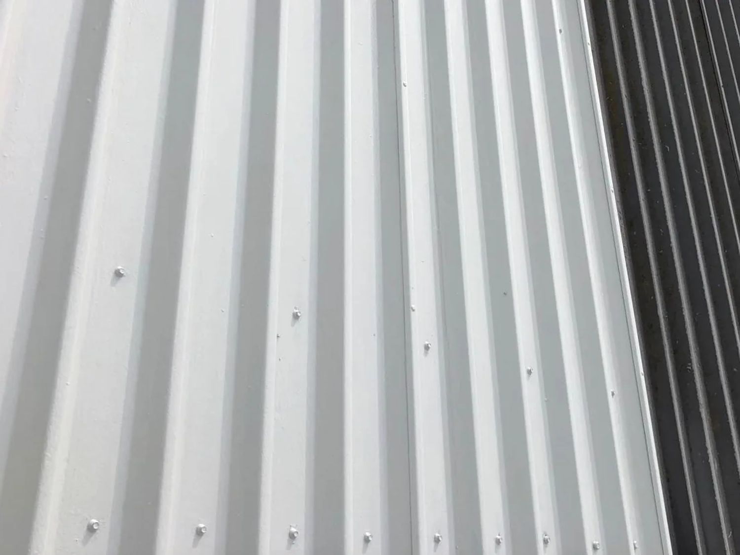 Half a metal roof coated white, the untreated sheets alongside still dark and weather-stained