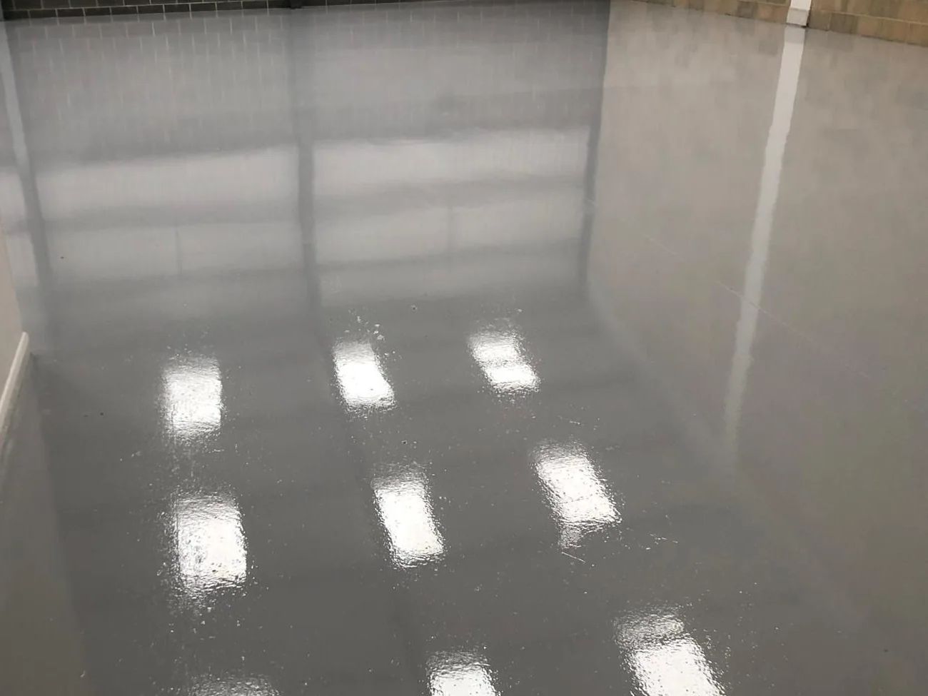 Poured grey resin floor across an industrial unit, with rooflights reflected in the finished surface