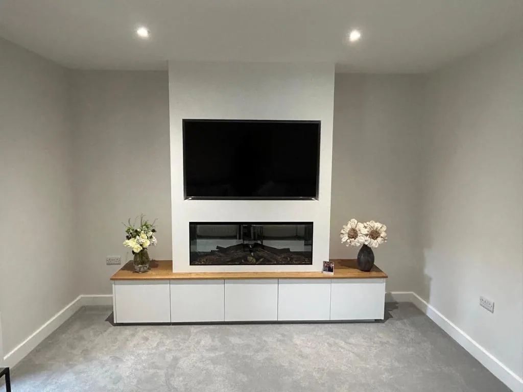 A long white media unit with an oak top and inset fire below a wall-mounted television