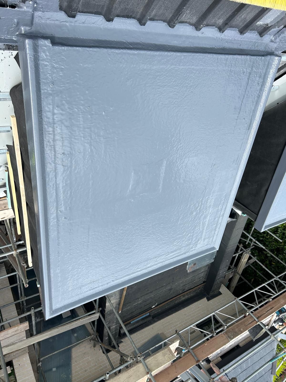 Overhead view of a liquid-coated flat roof beside a tiled roof and scaffolding