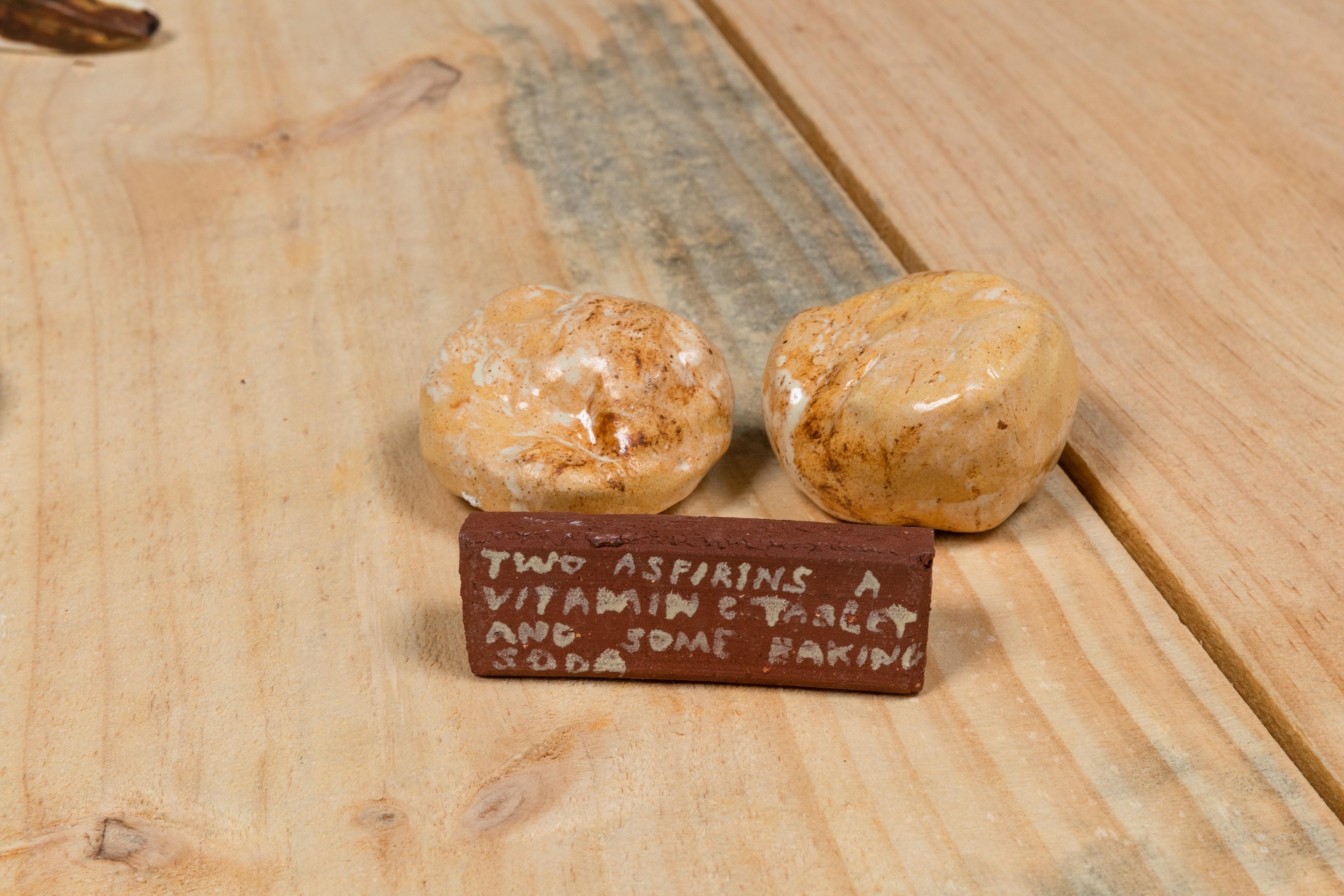 Two small ceramic items, with a additional ceramic sign stating 'two aspirins a vitamin c tablet and some baking soda', placed on wooden bench.