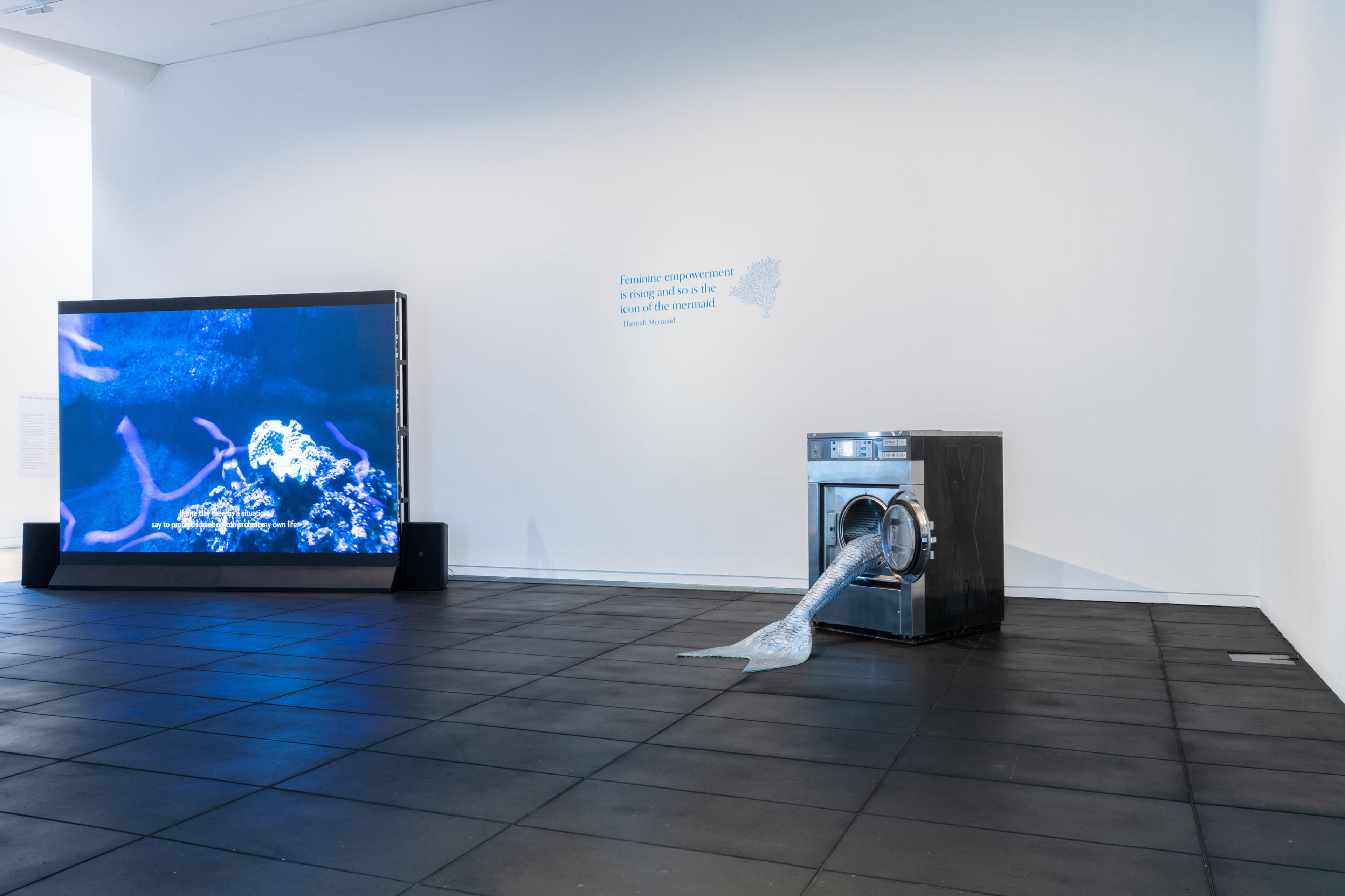 Lena Maria Thüring, Garden de la Paix, 2011, HD video, single channel, 16:9, colour, sound, 18 mins 47 secs; Olivia Erlanger, Pergusa (Gris), 2022, silicone and paint, commercial washing machine, courtesy of the artist and DM Office, New York. Installation view, Megan Dunn: The Mermaid Chronicles, Te Pātaka Toi Adam Art Gallery, Te Herenga Waka Victoria University of Wellington, 2022. Photo: Ted Whitaker