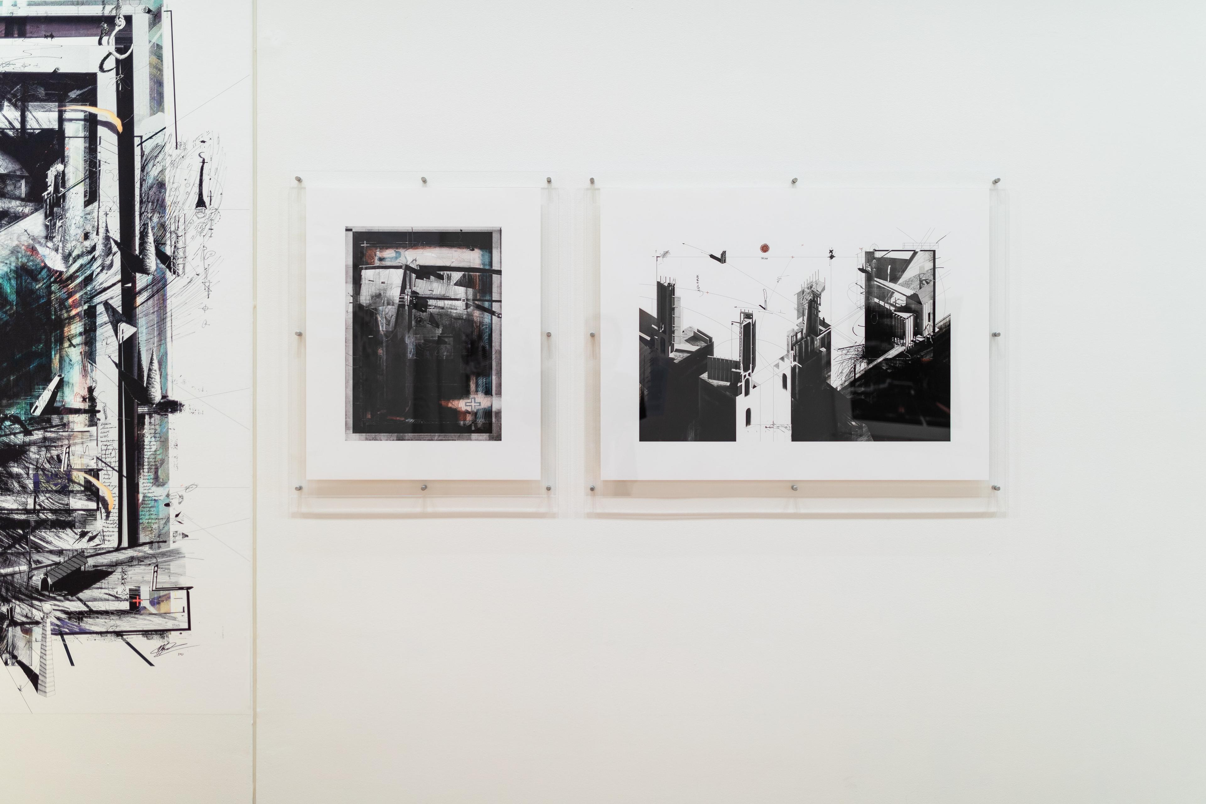 A straight on view of a white gallery wall with architectural images in perspex mounts, and cropped partly on the left is a larger print of a dark angular architectural drawing . Daniel K. Brown 