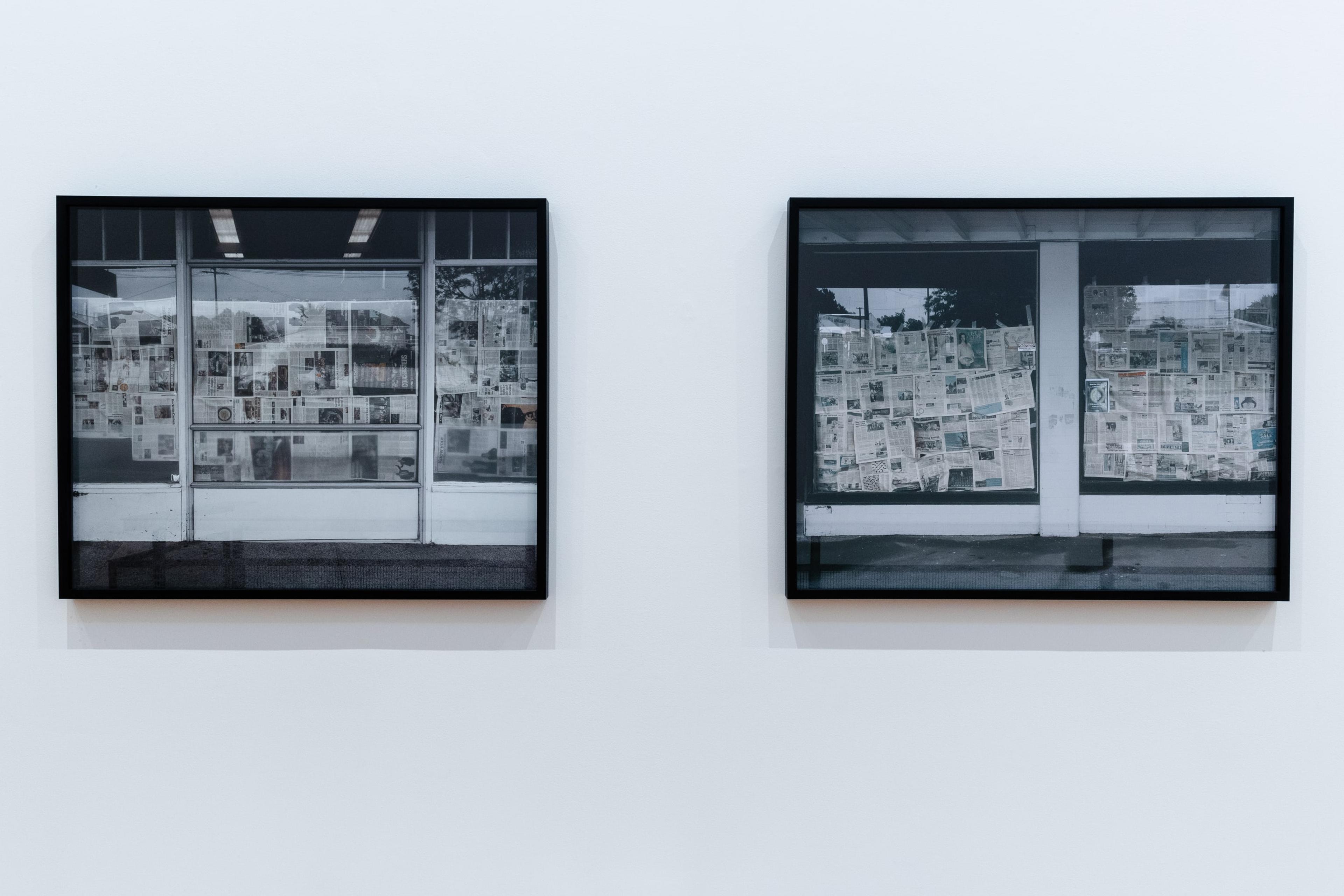 two framed black and white photographs of shop fronts with newspaper on their windows