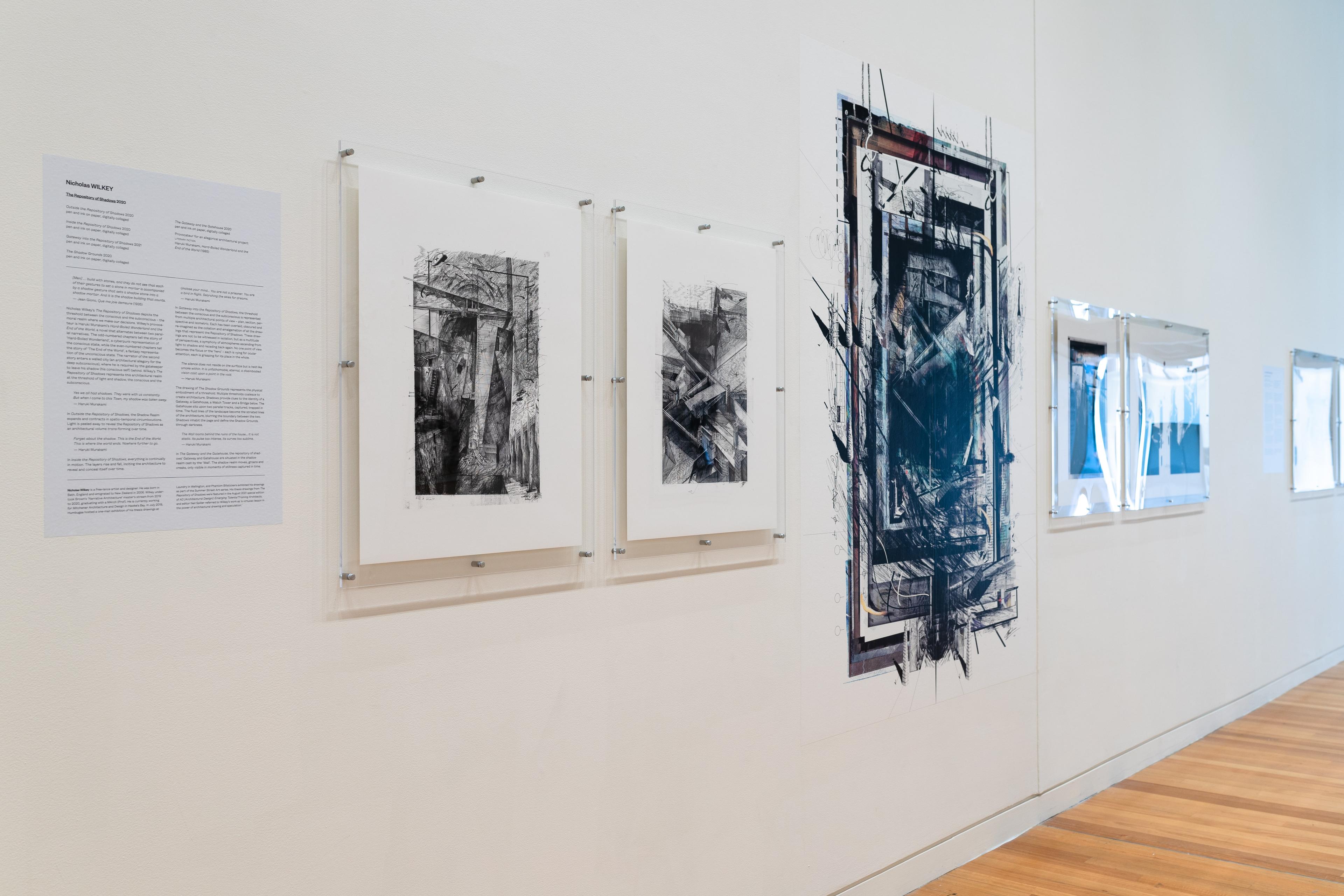 An oblique view of a gallery wall with text and 5 square architectural images in perspex mounts, and a larger print in the centre of a dark angular drawing. Daniel K. Brown 