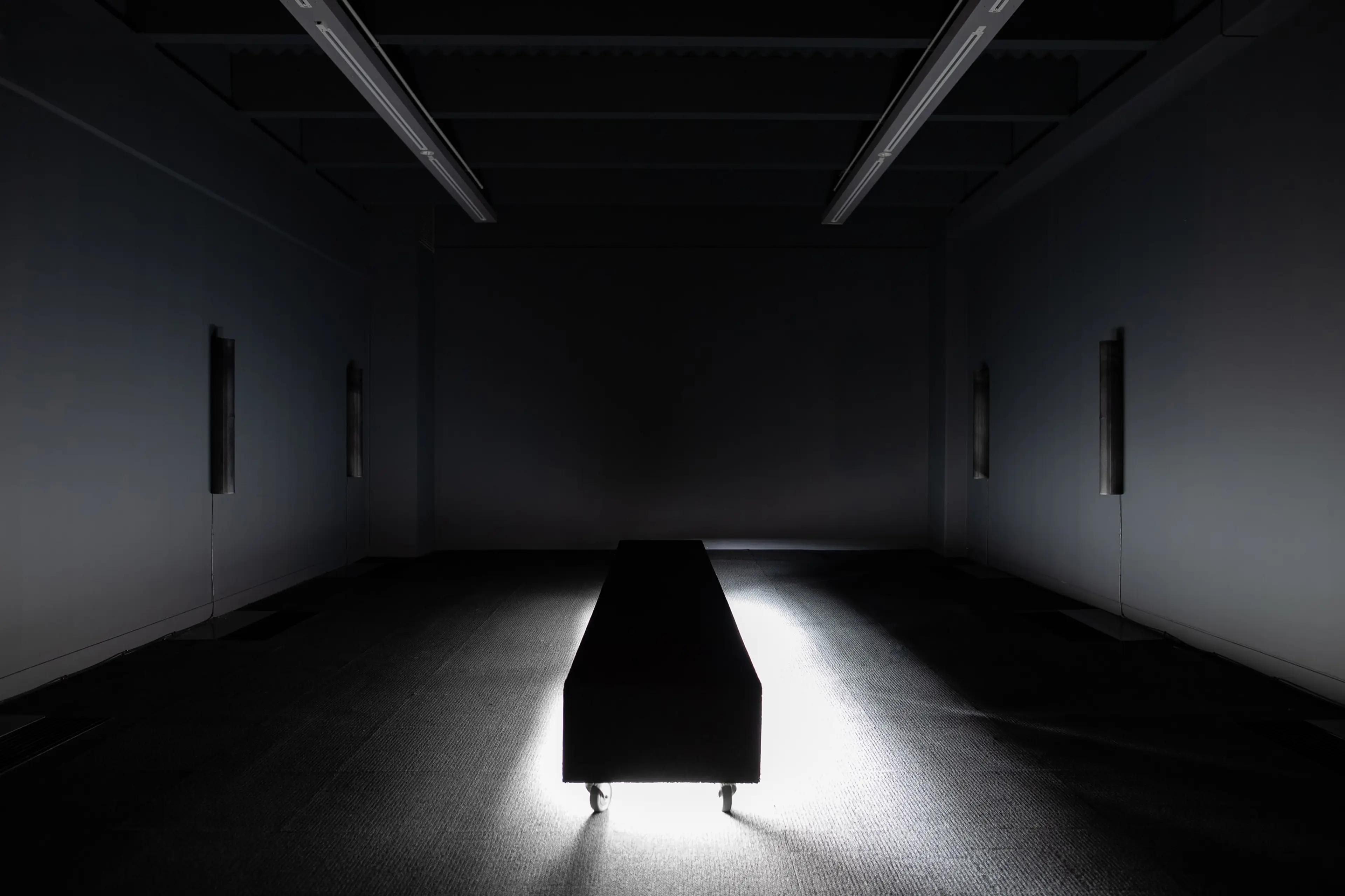 Gallery installation, room with no lights, central bench with light source underneath